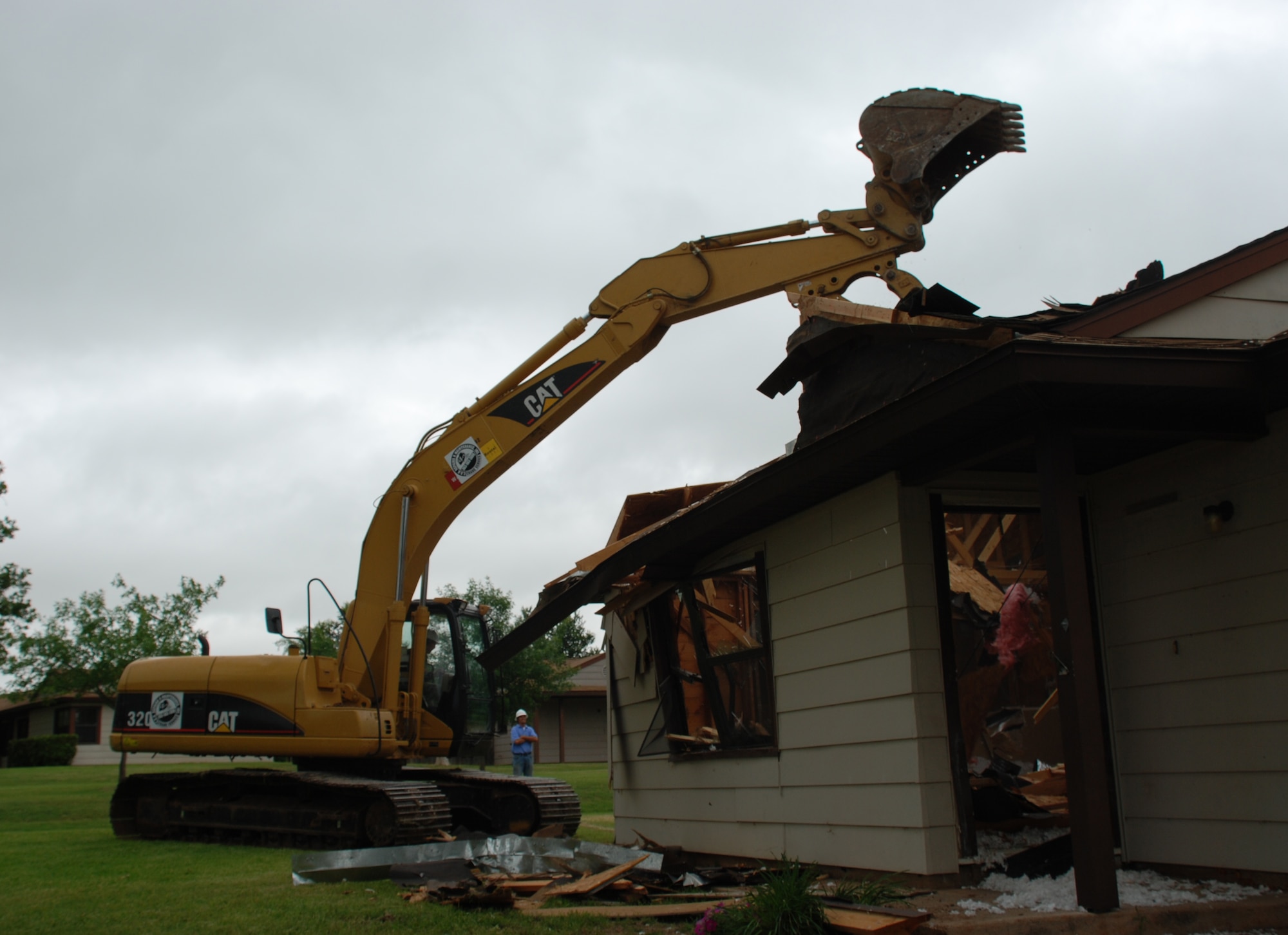 Brig. Gen. Richard Devereaux, behind the controls of an excavator, demolishes a Wherry housing home at the site of new officer and senior enlisted homes May 15. (U.S. Air Force photo/Airman 1st Class Jacob Corbin)