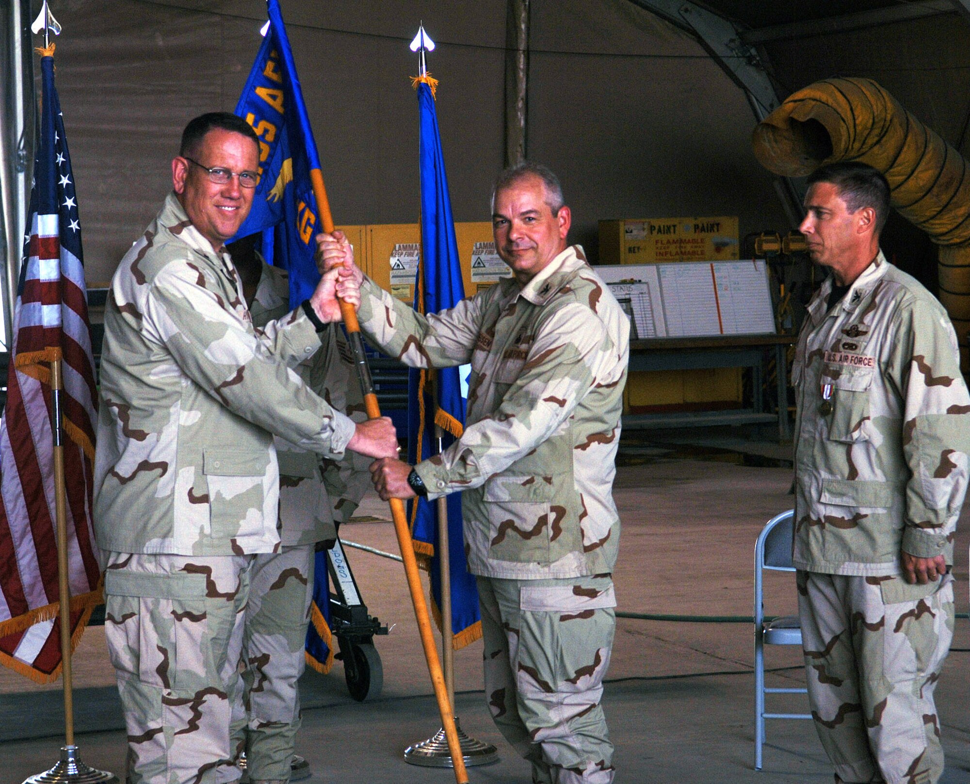 Col. John Theisen (middle), 455th Expeditionary Maintenance Group commander, accepts the 455th EMXG guidon from Brig. Gen. Bill Hyatt (left), 455th Air Expeditionary Wing commander during a change of command ceremony May 16. Col. Frank Stokes (right) relinquished command of the group to Col. Theisen during the ceremony. (photo by Staff Sgt. Craig Seals)