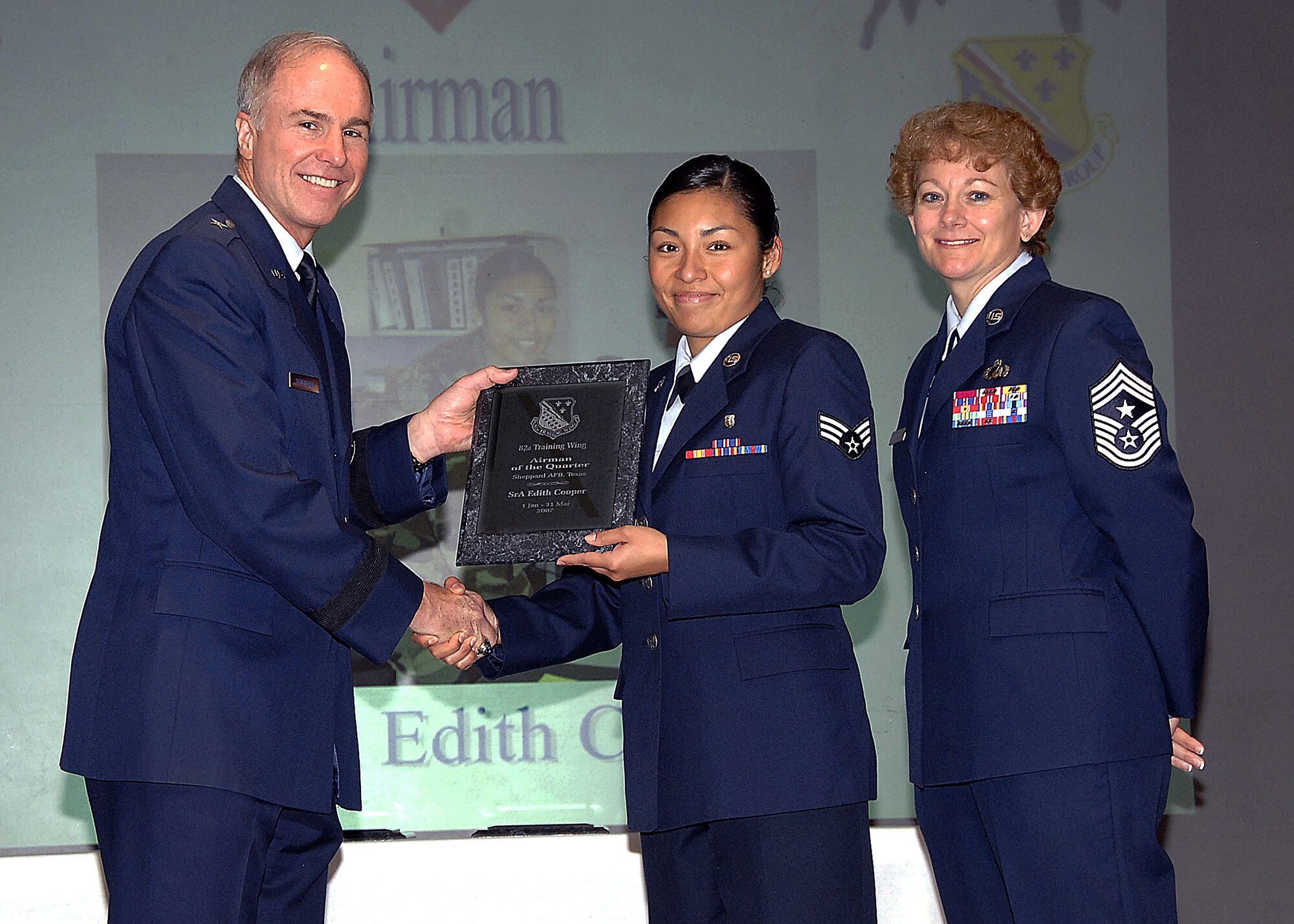Senior Airman Edith Cooper, center, of the 82nd Medical Operations Squadron accepts the Airman of the Quarter  award from Brig. Gen. Richard Devereaux, 82nd Training Wing commander, May 16 during a luncheon at the Sheppard Club. Airman Cooper was cited for her ability to save the squadron money by correcting a coding error for medical billing that saved the 82nd Medical Group $1.1 million. She also identified more than 350 items to return for credit, resulting in a return of $5,000 through the expired drug return program. In her free time, Airman Cooper tutored four junior high and high school students, as well as coached youth basketball and soccer teams. Also pictured with General Devereaux and Airman Cooper is 82nd TRW Command Chief Chief Master Sgt. Jeannie McLean. (U.S. Air Force photo/Harry Tonemah)