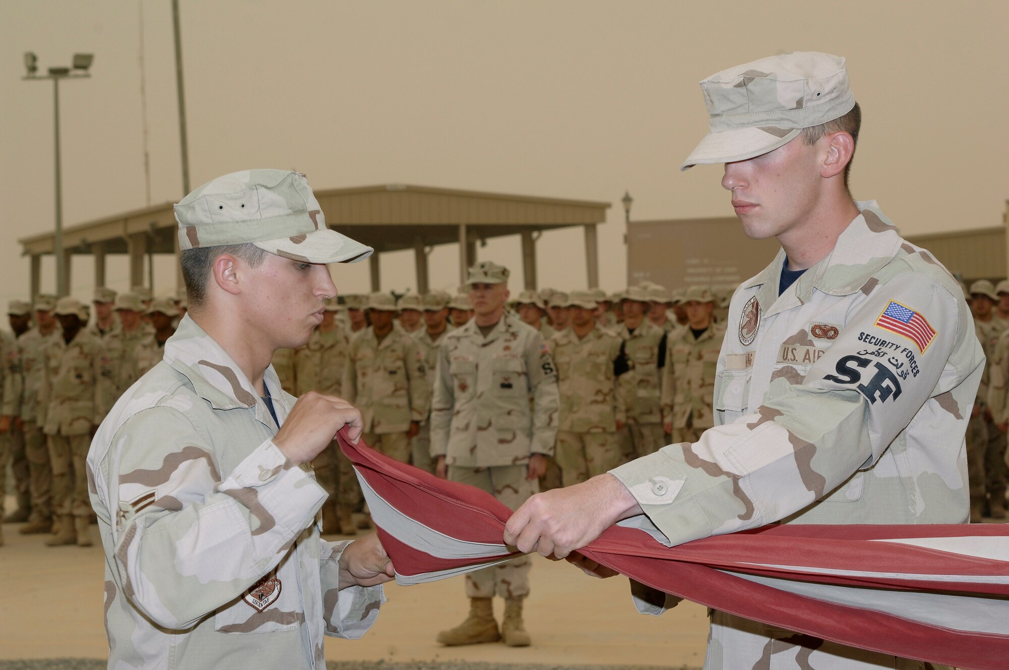 Airman 1st Class James Fowler (left) and Senior Airman Mark King (right), both of the 386th Expeditionary Security Forces Squadron, fold the flag, while Lt. Col. David Marttala  (background), 386th ESFS Commander, and the rest of the squadron look on, during a memorial retreat May 18, 2007. Security forces Airmen performed the ceremony in honor of National Police Week. The 386th ESFS also paid a special tribute to Staff Sgt. John Self, a security forces dog handler killed in action May 14. (U.S. Air Force photo by Staff Sgt. Raymond Mills)