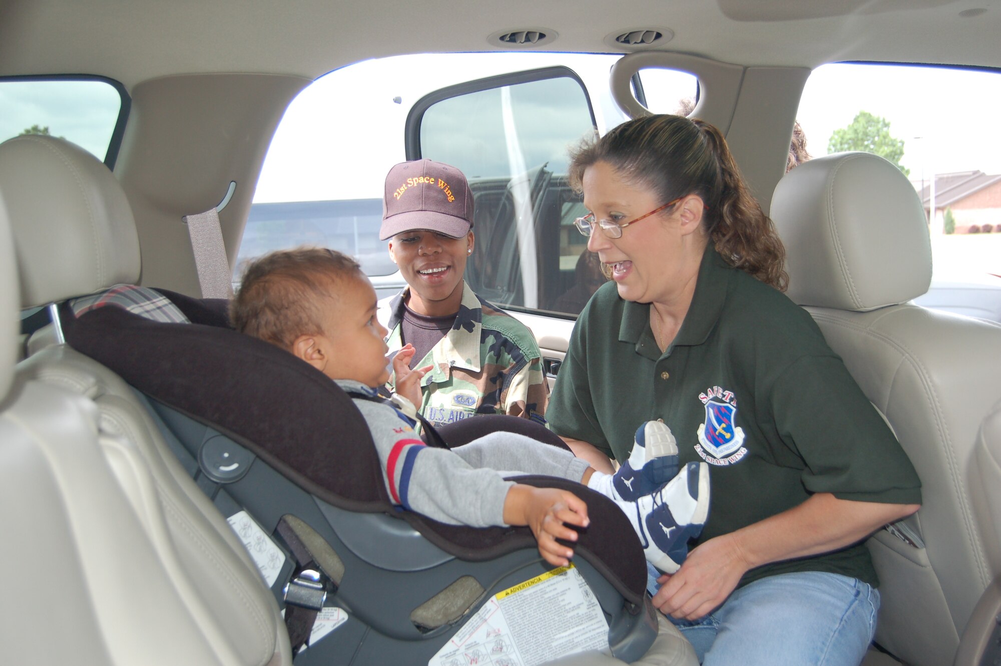 Tech. Sgt. Janet Doyle demonstrates how to properly secure 18-month-old Cayden Rizzitello in his car seat, while Staff Sgt. Michelle Stewart looks on. Sergeant Doyle, a member of the 21st Space Wing’s safety office, and other servicemembers held a free car seat safety check May 23. The base holds the check twice a year as part of the worldwide Safe Kids program, an initiative aimed at preventing unintentional childhood injuries. (U.S. Air Force photo by Corey Dahl)