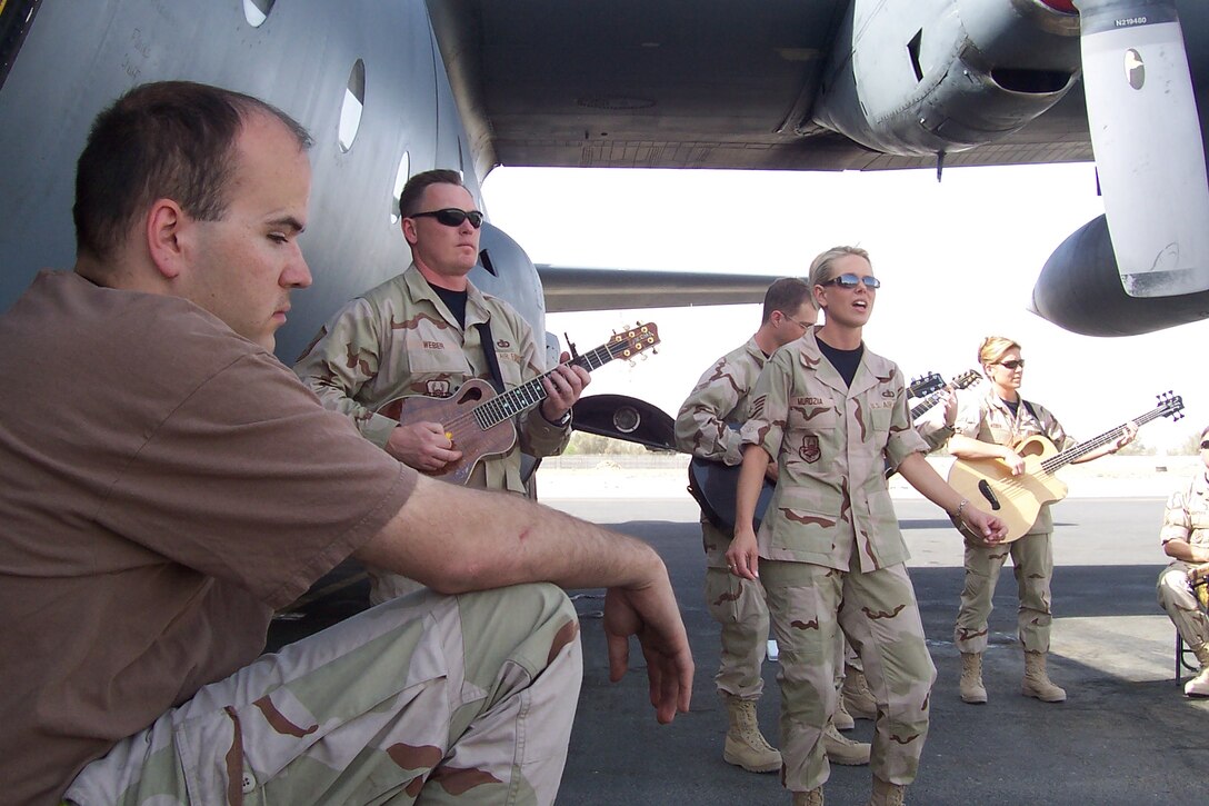 An aircraft mechanic takes a break form the hot Kuwaiti sun while lead vocalist Staff Sergeant Lara Murdzia and Night Wing perform the Sara Evans hit, “A Real Fine Place to Start”. Night Wing is a part of the USAF Heartland of America Band.