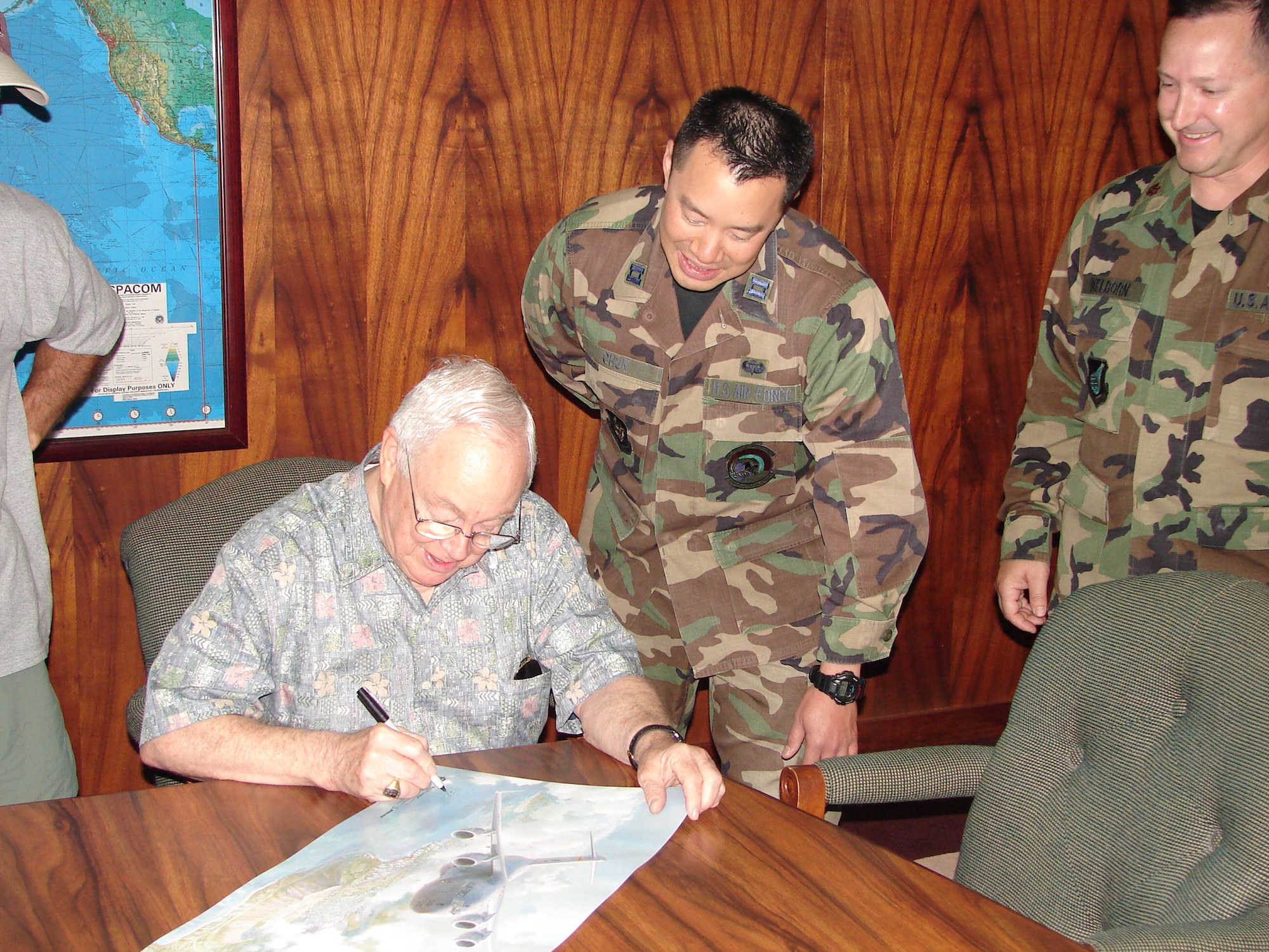 HICKAM AIR FORCE BASE, Hawaii -- Artist Keith Ferris autographs a copy of his painting "Waikiki Sunrise" for Capt. David Chun at Pacific Air Forces Headquarters May 23.  "Waikiki Sunrise" depicts a new era in airlift for the Pacific -- the first C-17 Globemaster III squadron based outside the continental United States. This is Mr. Ferris' 59th contribution to the Air Force Art Collection over the course of 46 years. The painting will be kept here on permanent display in the PACAF headquarters. (Air Force photo by Maj. Brad Jessmer)