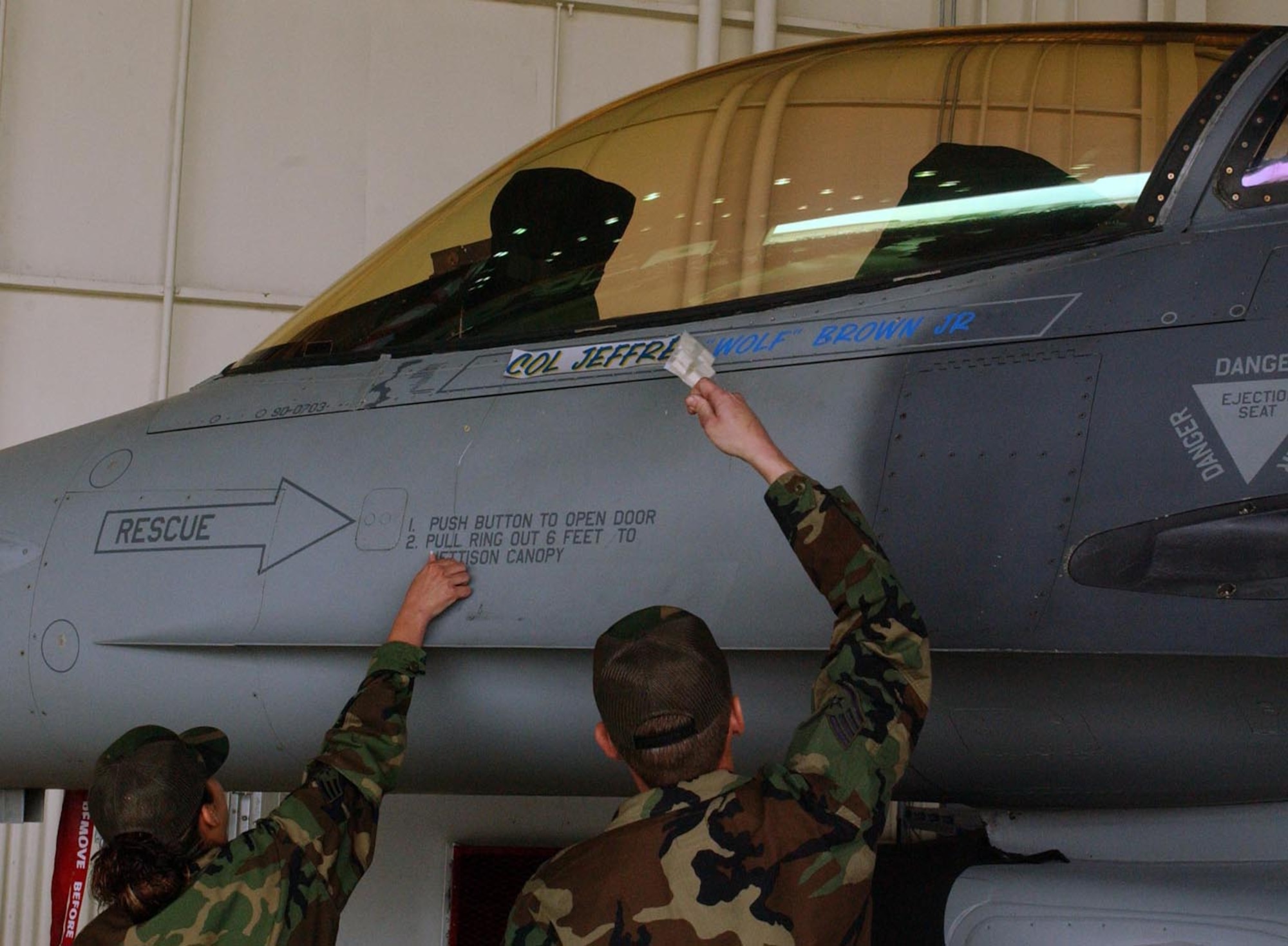 Senior Airman Nicole Pena and Staff Sgt. Derek Griggs, both F-16 Crew Chiefs from the 80th Aircraft Maintenance Unit, pull a magnetic strip off of the 8th Fighter Wing flagship aircraft to expose Colonel Charles "Wolf" Brown's name dedicating it to him while under his command for the next year. Col. Brown took command of the 8th FW during a ceremony in Hangar 3 May 25. (U.S. Air Force photo/Senior Airman Steven Doty)                               