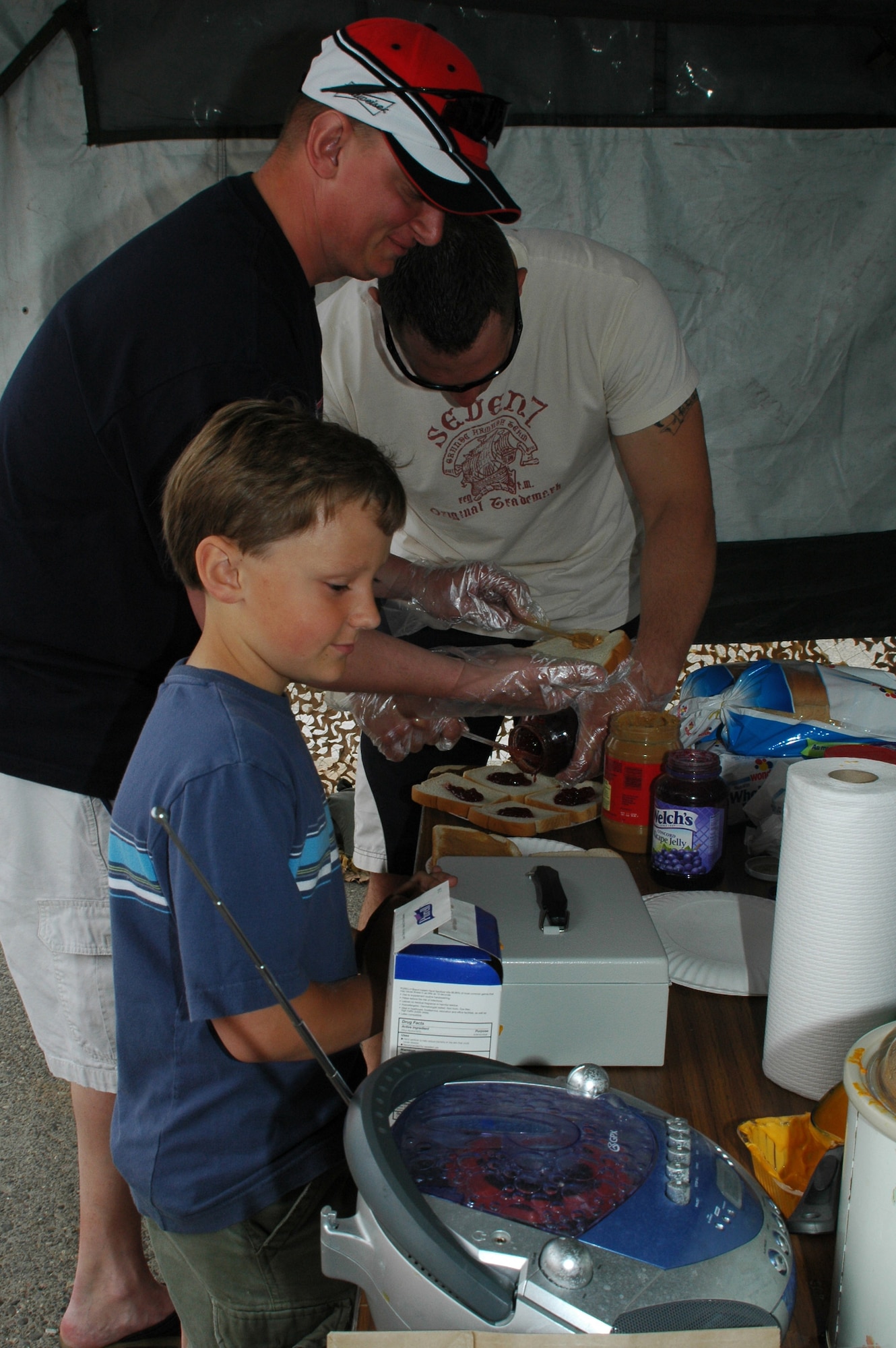 Little Warrior Kyle, 8, along with Tech. Sgt. Andy Patton and Staff Sgt. Michael Pease, 341st Security Forces Squadron members, man the peanut butter and jelly sandwich booth at the open house and air show at Malmstrom Air Force Base May 20. (U.S. Air Force photo by Airman 1st Class Emerald Ralston)