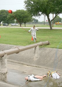 A Team Lackland firefighter responds to a severe weather military exercise May 21 at Lackland Air Force Base, Texas, by slinging a floatation device into a ditch in an effort to save two dummies depicting children swept away in heavy rain. Coincidentally, the exercise was interrupted by a real world severe weather situation which lasted much of the day. (USAF photo by Robbin Cresswell)