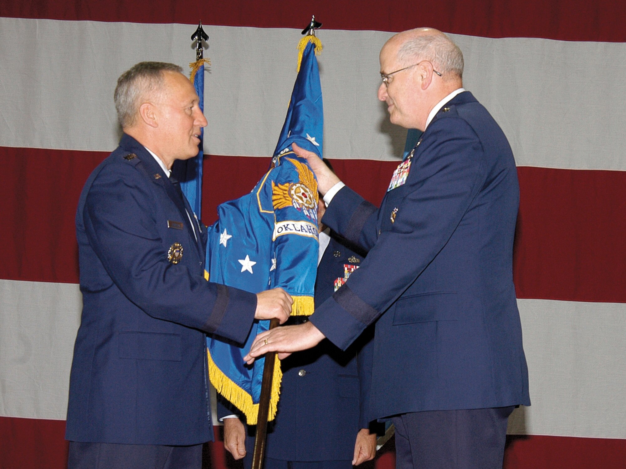 Gen. Bruce Carlson, left, passes command of the Oklahoma City Air Logistics Center to Maj. Gen. Loren M. Reno May 30.  The commander of Air Force Materiel Command passed the guidon in a traditional ceremony before approximately 1500 workers, civic and military leaders and retired Tinker commanders gathered in a Bldg. 3001 aircraft dock. (Air Force photo by Margo Wright)