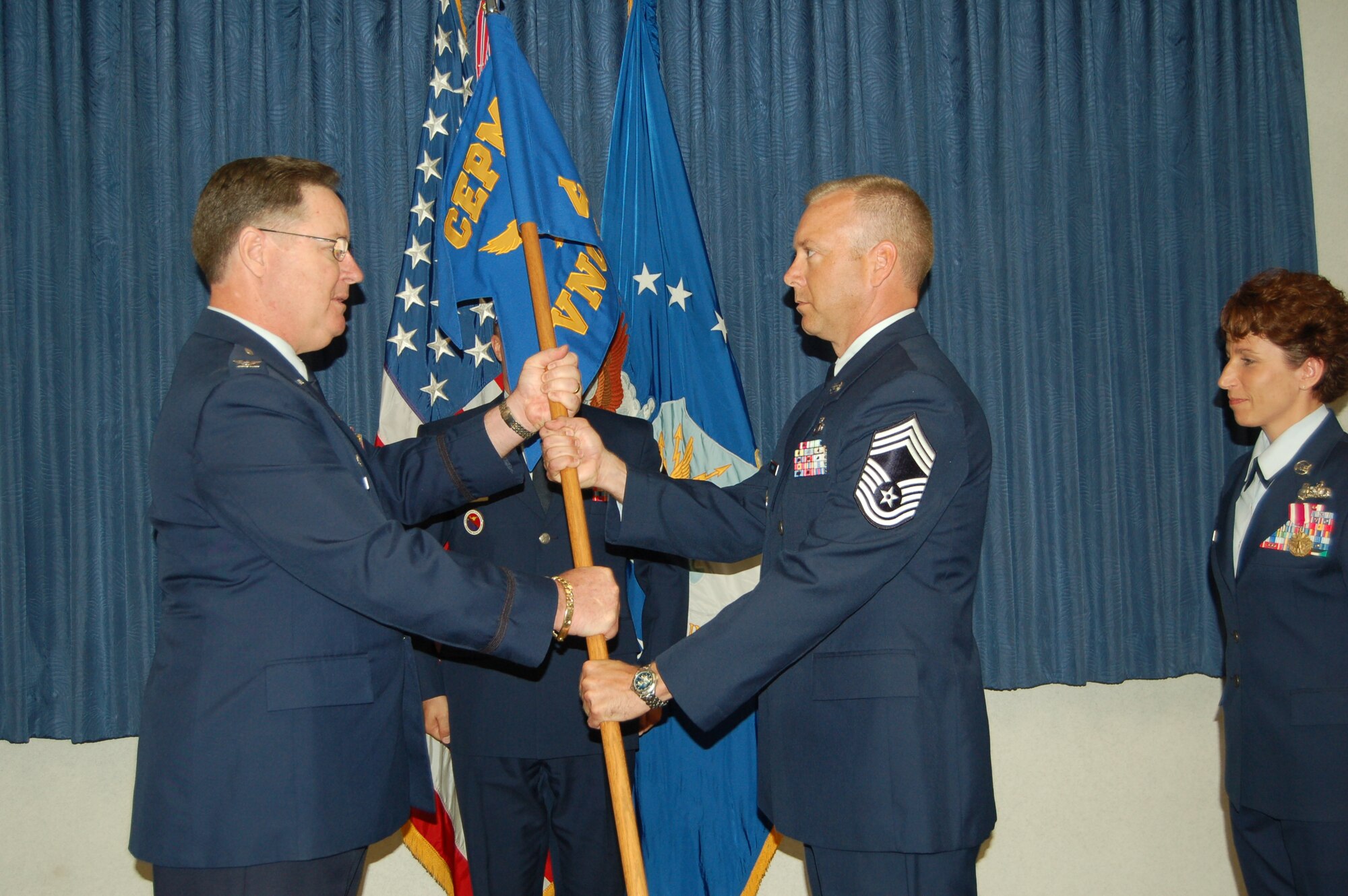 Col. Albert Bowley, commander of the College for Enlisted Professional Military Education, passes leadership of the Vosler NCO Academy to Chief Master Sgt. Thomas Young. Looking on is the outgoing VNCOA leader, Chief Master Sgt. Cari Kent. (U.S. Air Force photo by Corey Dahl)