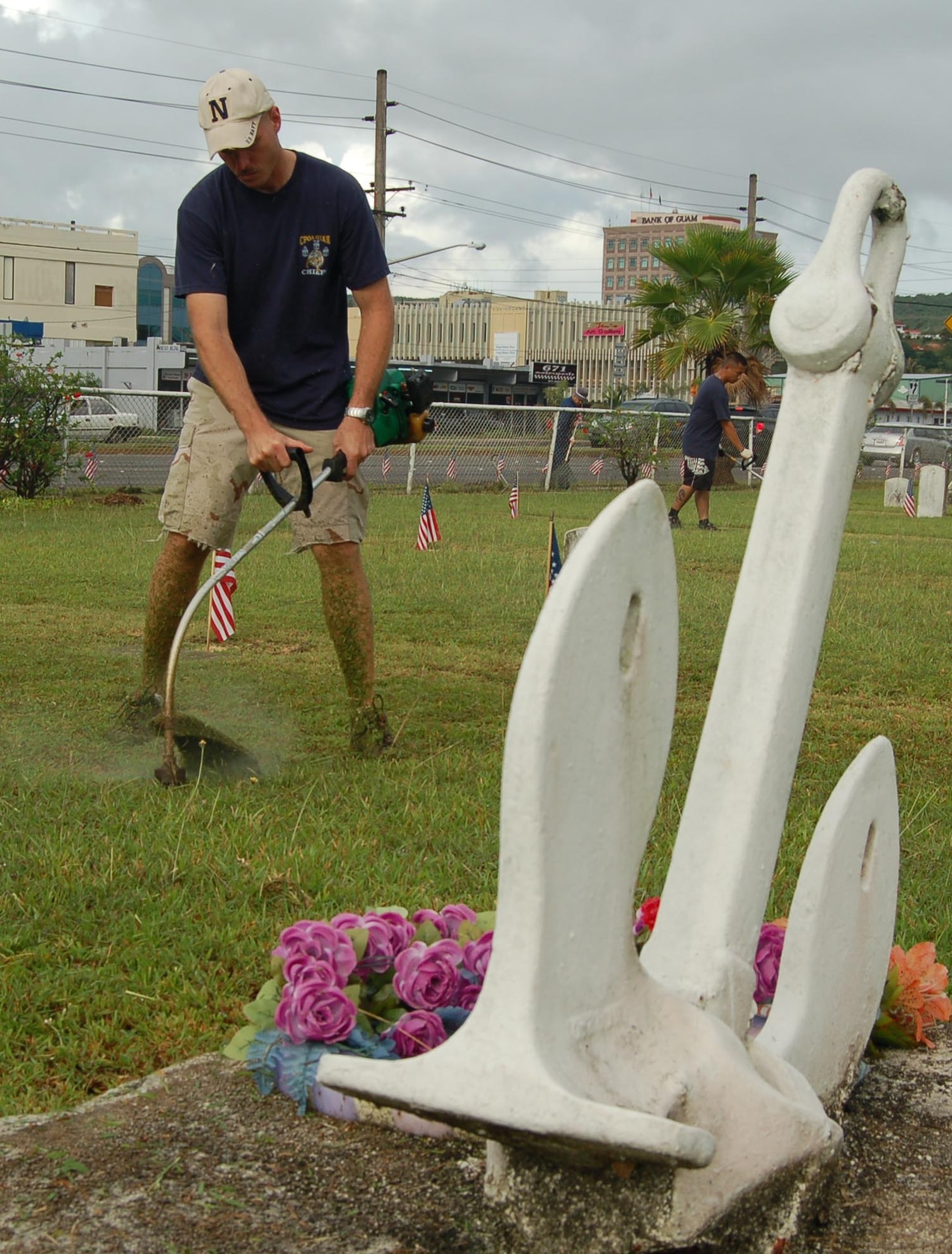 SKC Michael Callang trims the lawn near an anchor which stands in tribute to the sacrifices of the fallen Sailors and Marines who lay in rest at the Agana Cemetery. SKC Callang and several other Sailors from Helicopter Sea Combat Squadron-Two Five cared for the Agana Cemetary May 25 as their way of honoring the men and women buried there - their personal tribute to bring in the Memorial Day weekend.  (Photo by Tech. Sgt. Brian Bahret/36th Wing Public Affairs)