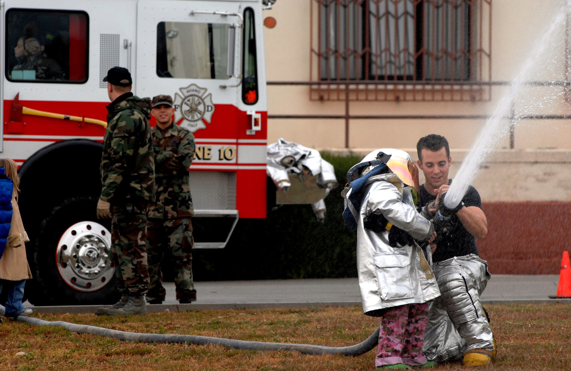 Airman 1st Class Christopher Gonzalez helps 2nd grader Alexa Arancubia use an attack hose during a children's deployment day Oct. 24 at Aviano Air Base, Italy. Alexa is the daughter of Tech. Sgt. Abel Arancubia and Jennifer Arancubia. Airman Gonzalez is a firefighter with the 31st Civil Engineer Squadron. (U.S. Air Force photo/Airman 1st Class Nathan Doza)