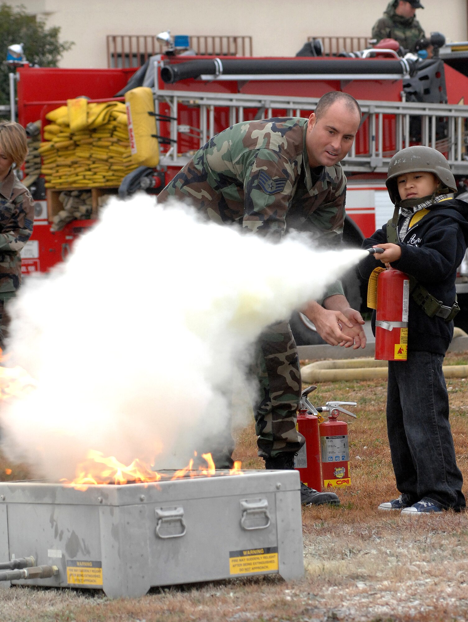 Staff Sgt. Michael Johns helps 2nd grader Jacob Calderon use a fire extinguisher during a children's deployment day Oct. 24 at Aviano Air Base, Italy. Sergeant johns is a firefighter with the 31st Civil Engineer Squadron. Jacob is the son of Tech. Sgt. Ridolfo Calderon and Venus Calderon. (U.S. Air Force photo/Airman 1st Class Nathan Doza)