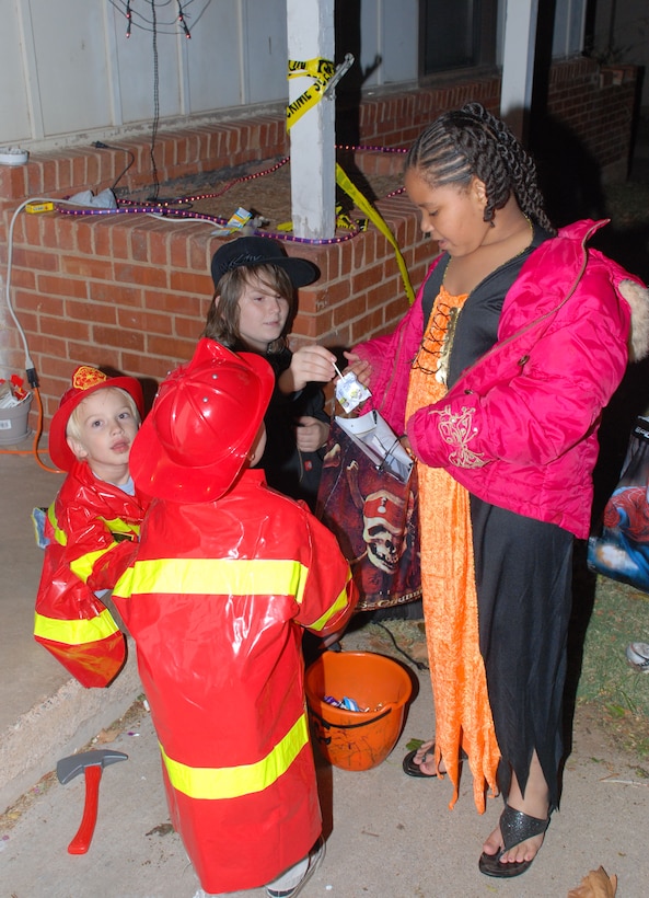 Henry and Peter Campbell (left) sons of Private Dustin Campbell, and Dylan Worth, son of Petty Officer 2nd Class Angela Worth, hand out candy to Alexis Pryor, daughter of Evelyn Gomez Oct. 31 in Wherry Housing. (U.S. Air Force photo/Airman 1st Class Jacob Corbin)