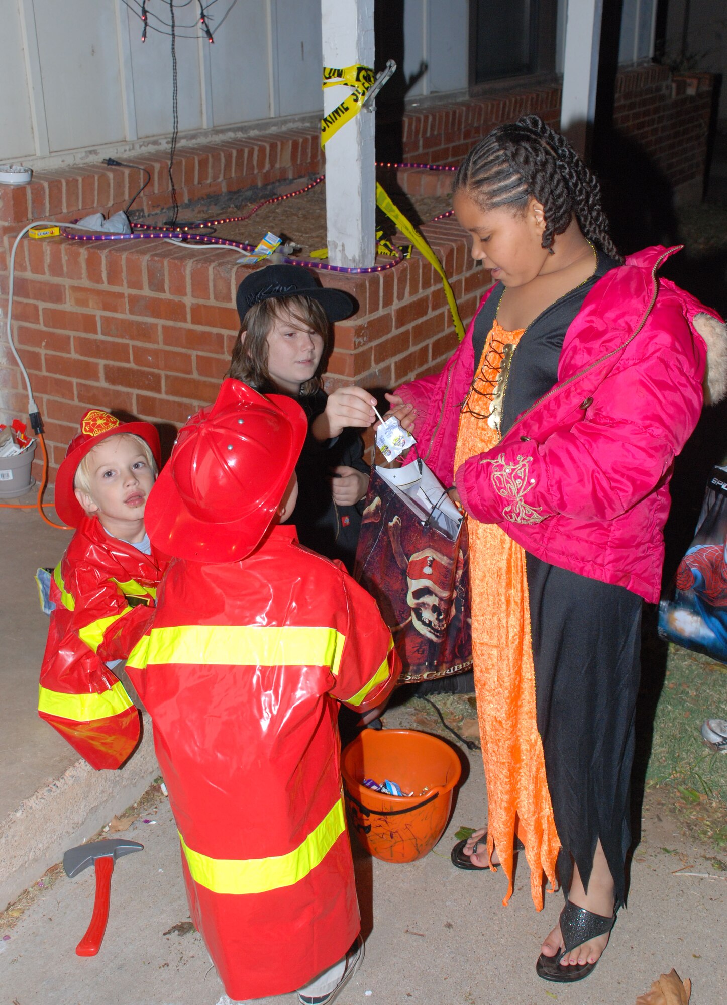 Henry and Peter Campbell (left) sons of Private Dustin Campbell, and Dylan Worth, son of Petty Officer 2nd Class Angela Worth, hand out candy to Alexis Pryor, daughter of Evelyn Gomez Oct. 31 in Wherry Housing. (U.S. Air Force photo/Airman 1st Class Jacob Corbin)
