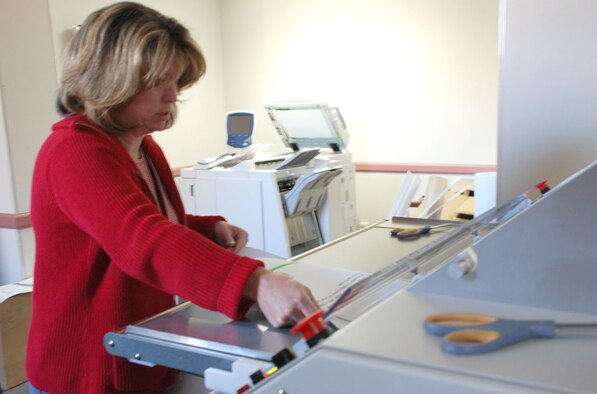 Mary Fahrer, a graphic designer with Warren’s multimedia center, assists portions of her project through a laminator Oct. 25. In addition to a lamination machine, the multimedia office has several large printers with varied powers and functions for different types of products (Photo by Airman 1st Class Alex Martinez).