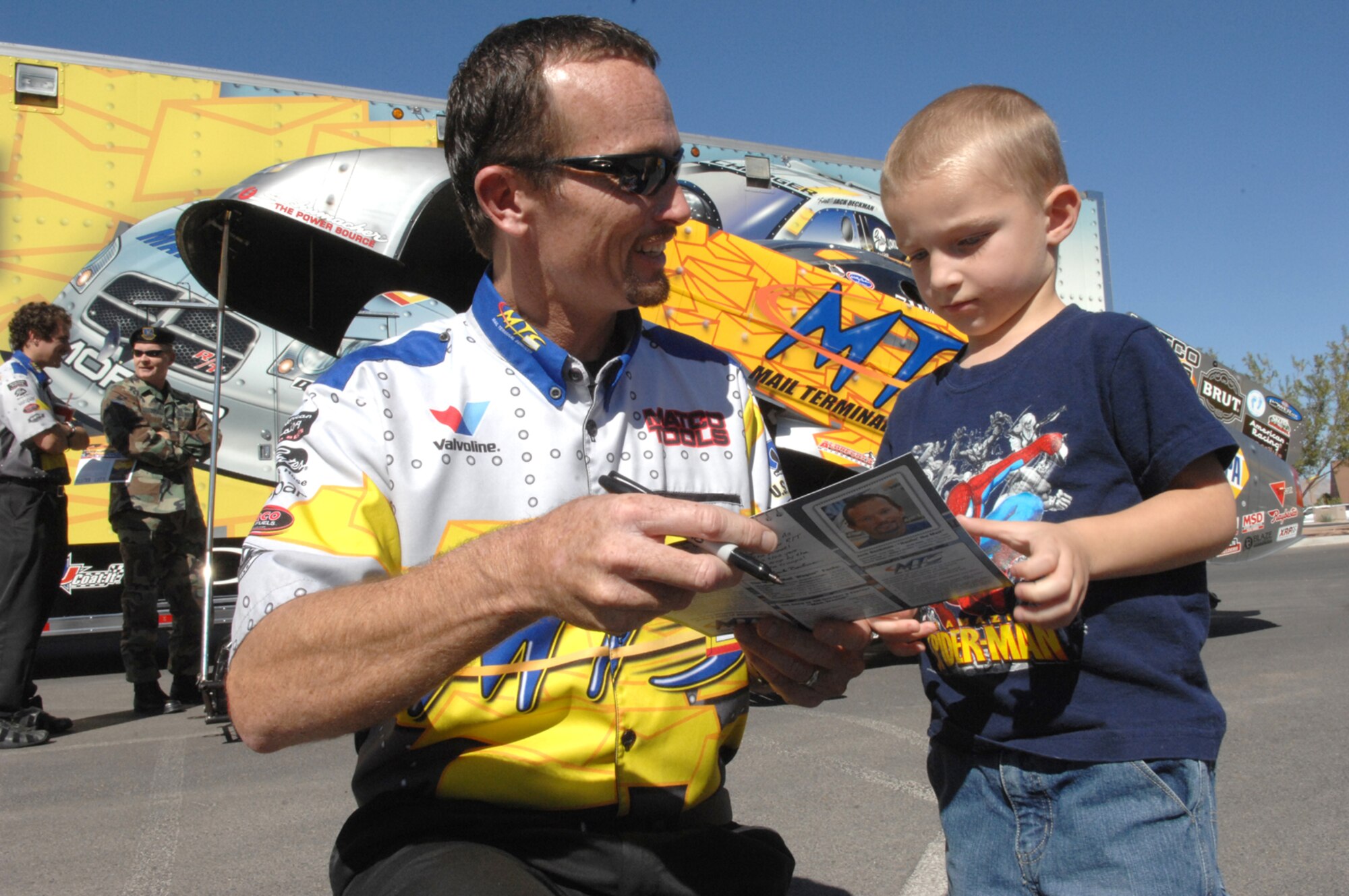 Former Air Force Sgt. Jack Beckman, now turned Funny racecar driver for Don Schumacher Racing, autographs a souvenir for Nick Millikan, 4, Oct. 24 at the Nellis Base Exchange parking lot. Jack Beckman and other National Hot Rod Association drivers stopped by Nellis for a military community “meet-and-greet” before racing in Las Vegas. (U.S. Air Force Photo by Senior Airman Larry E. Reid Jr.)