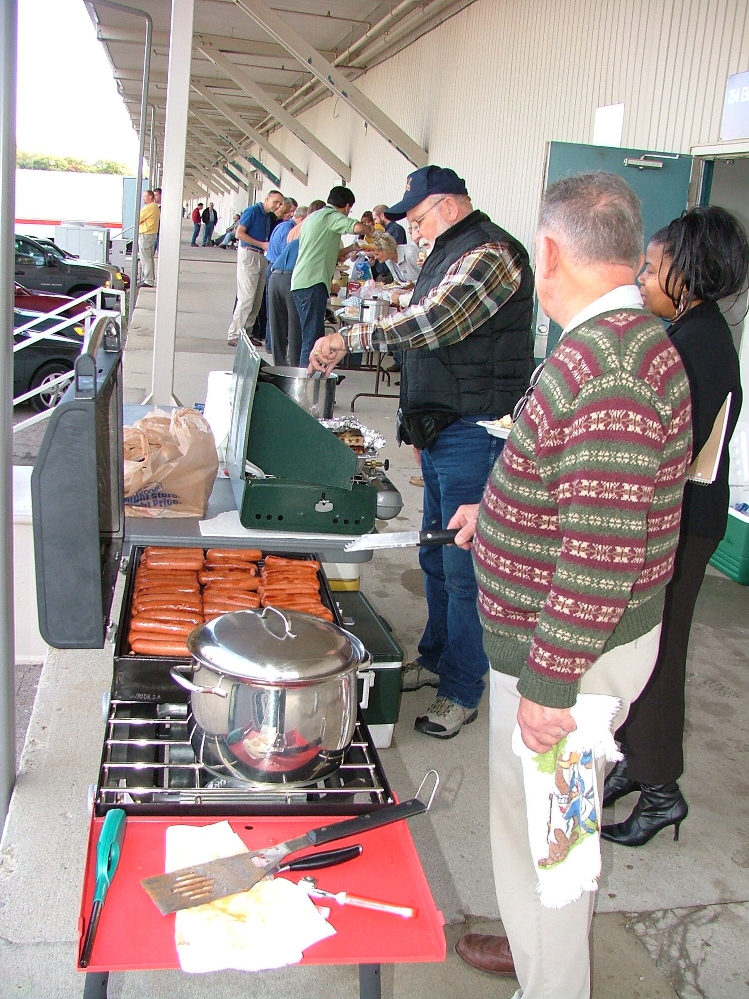 Individuals line up for “Dogs on the Dock.” Vic Cookin foreground, and Joe Ruewer work the grill. Teamwork at its best! (Courtesy photo by Dick Smith)