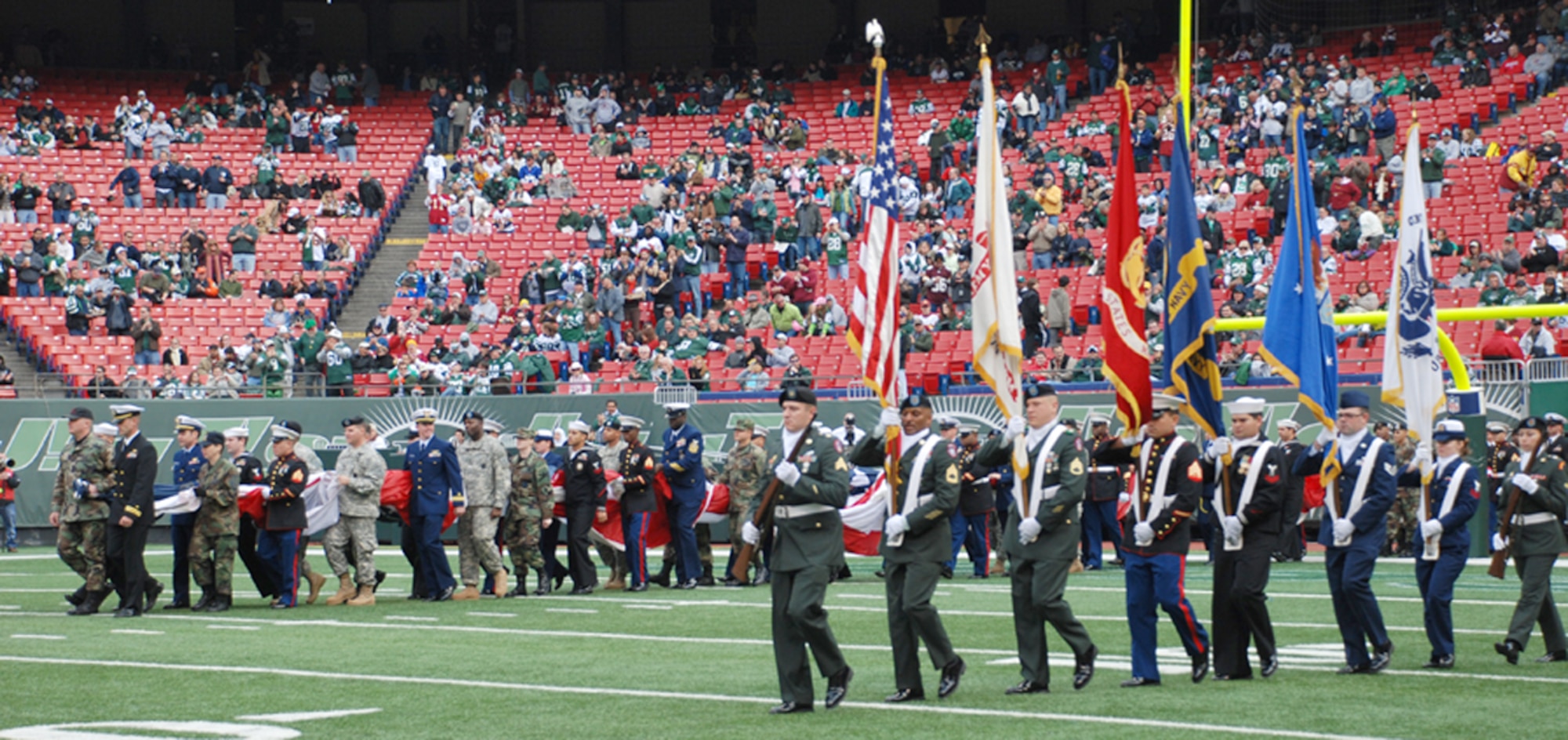 McGuire Airmen and members of each of the other four military services enter the stadium at the Nov. 4 NFL game between the N.Y. Jets and Washington Redskins. The servicemembers unfurled an enormous American Flag as part of the Jets' eighth annual Military Appreciation Day. Fifteen Team McGuire members participated in the event, which honored all servicemembers, as well as Navy Lt. Michael Murphy, a SEAL who lost his life in Afghanistan two years ago and was posthumously awarded the Medal of Honor. (U.S. Air Force photo / Airman 1st Class Rebekah Phy)