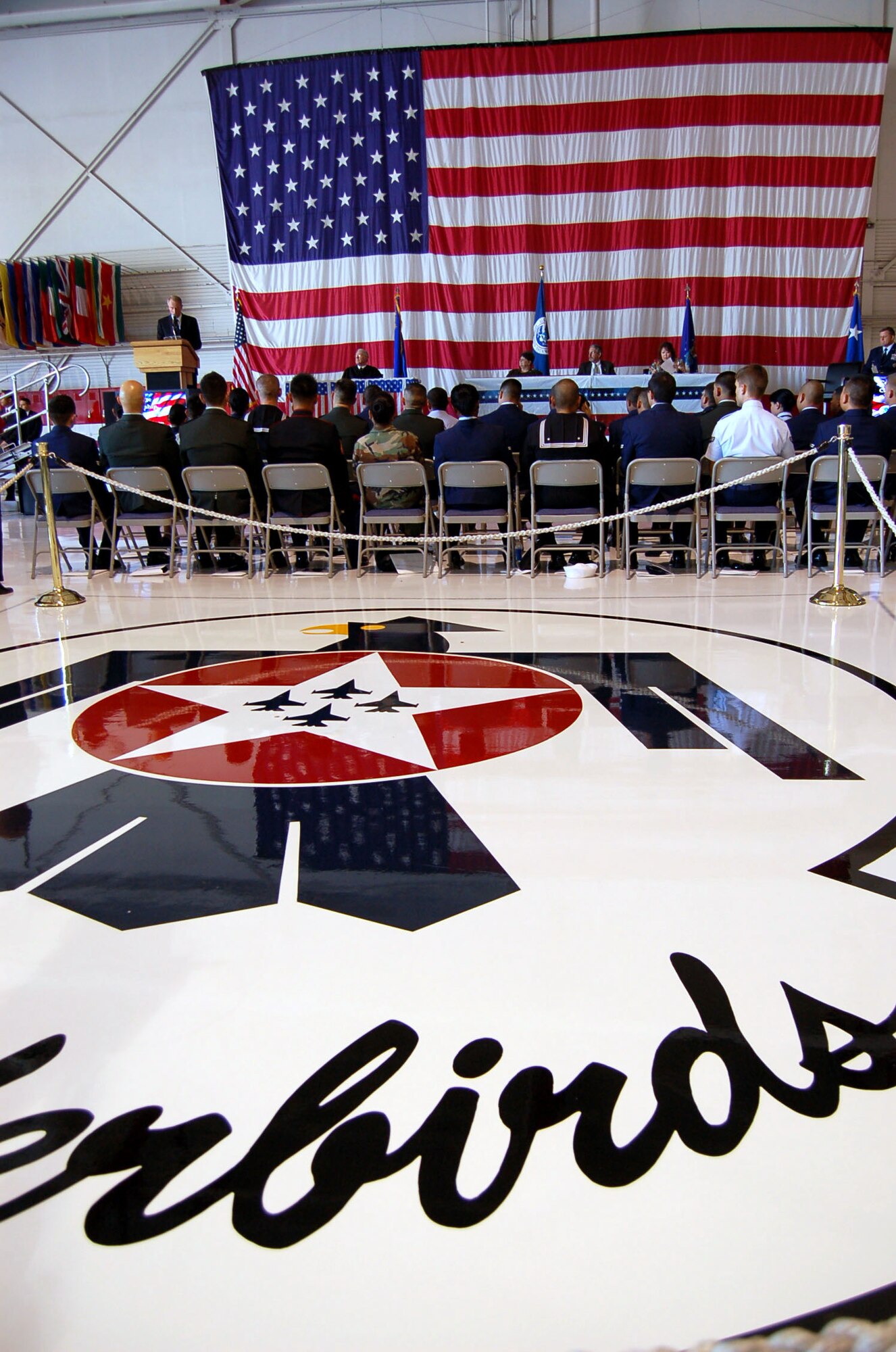Thomas C. Parr speaks to attendees at the naturalization ceremony next to the Air Force Thunderbirds Air Demonstration Squadron logo on the team's hangar floor Nov. 6 at Nellis Air Force Base, Nev. Mr. Parr is the chief of staff for the U.S. Citizenship and Immigration Services. Airman 1st Class Olga Bilobol was one of 33 military members to participate in the event, which is the last step in the process of becoming an American citizen. The new citizens included representatives from all the branches of the military. The event was part of the base's Heritage to Horizons celebration of the Air Force's 60th Anniversary (U.S. Air Force photo/Staff Sgt. Jeremy Larlee)