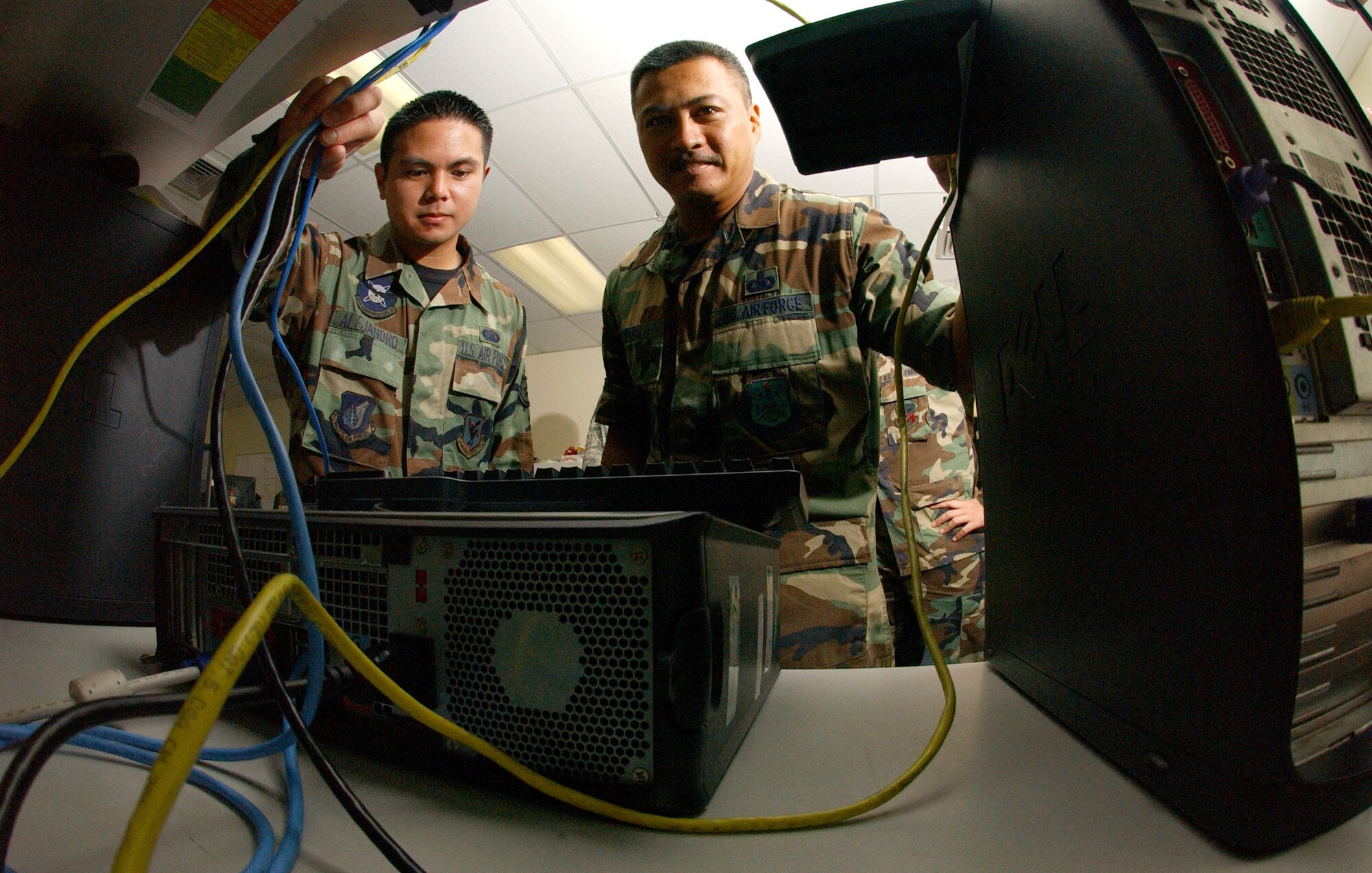 Senior Master Sgt. Vincent Devera (right) and Staff Sgt. Matthew Alejandro are framed by computer components at the Andersen Air Force Base, Guam, network control center.  Sergeant DeVera, the chief of the local network control center, was responsible for bringing a team of Airmen together who deployed here from various organizations and fusing them into one cohesive unit. (U.S. Air Force photo/Senior Airman Brian Kimball)