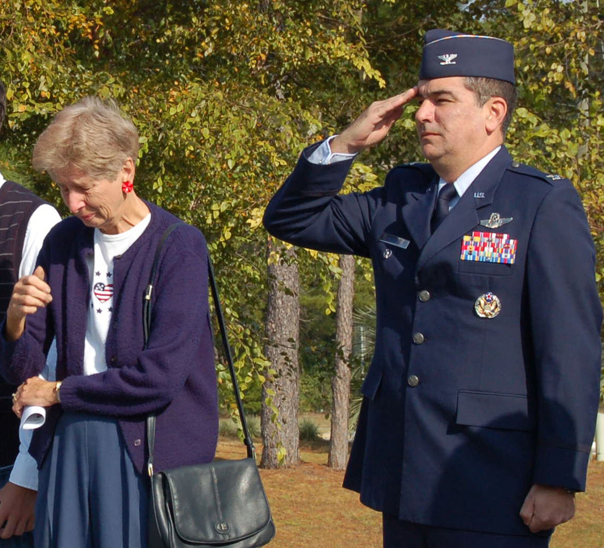 Col. Mick Guthals, 53d Wing vice commander, salutes as Darlene Kampworth remembers her husband during the playing of taps at the Veterans Day ceremony at the Heritage Gardens Cemetary in Niceville, Nov. 12.  Colonel Guthals was the guest speaker at the ceremony.  Mrs. Kampworth's husband Donald served as a meterologist in the Air Force and is buried at Heritage Gardens.  Her two sons also served in the military.  Air Force photo by Staff Sgt. Samuel King Jr.