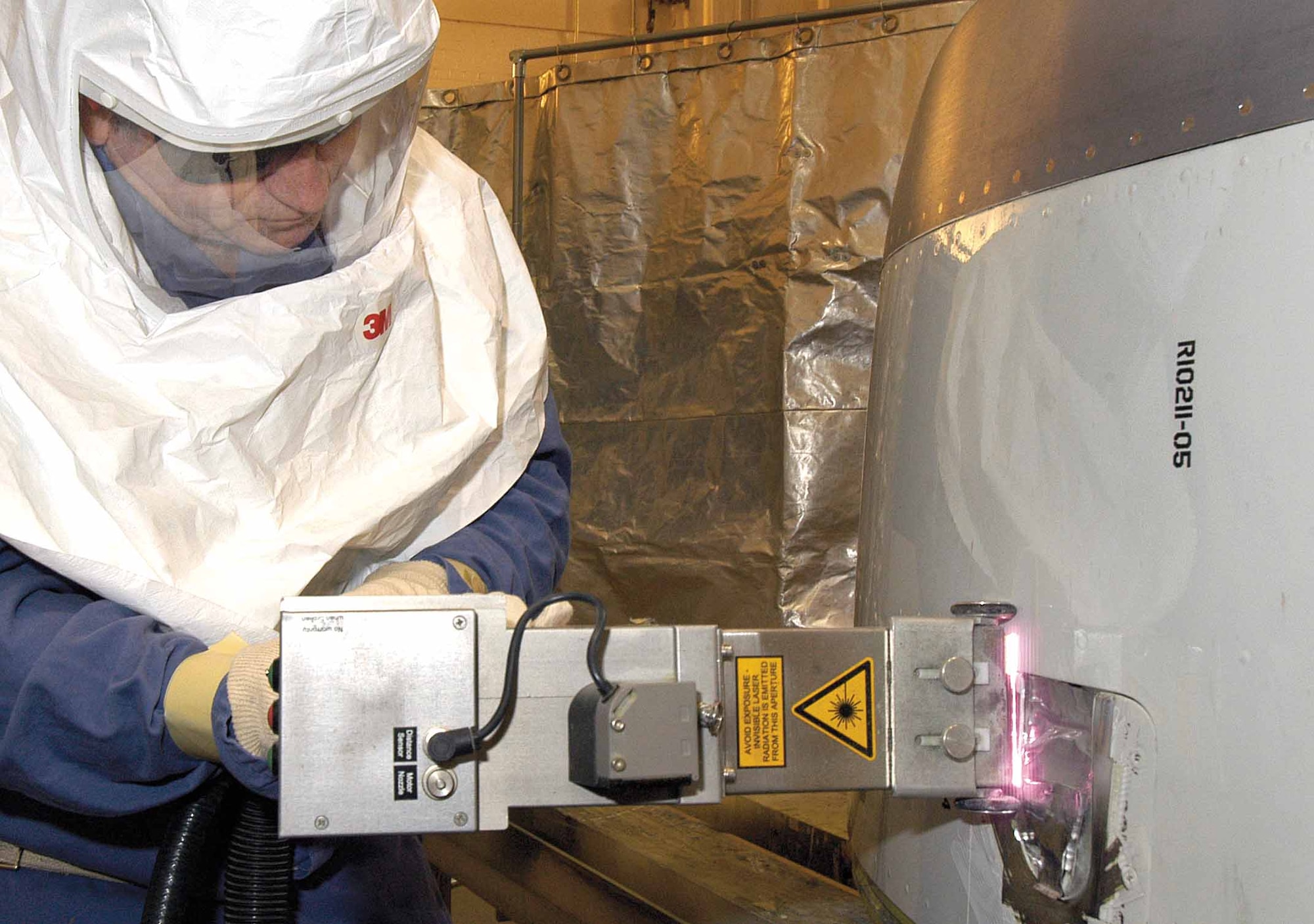 Laser operator Alvin Howard removes paint from E-3 nose cowling openings using a hand-held laser. The new process replaces less friendly liquid removers used for the many small areas on aircraft components and looks promising for wider aircraft paint removal uses in the future. (Air Force photo by Margo Wright)