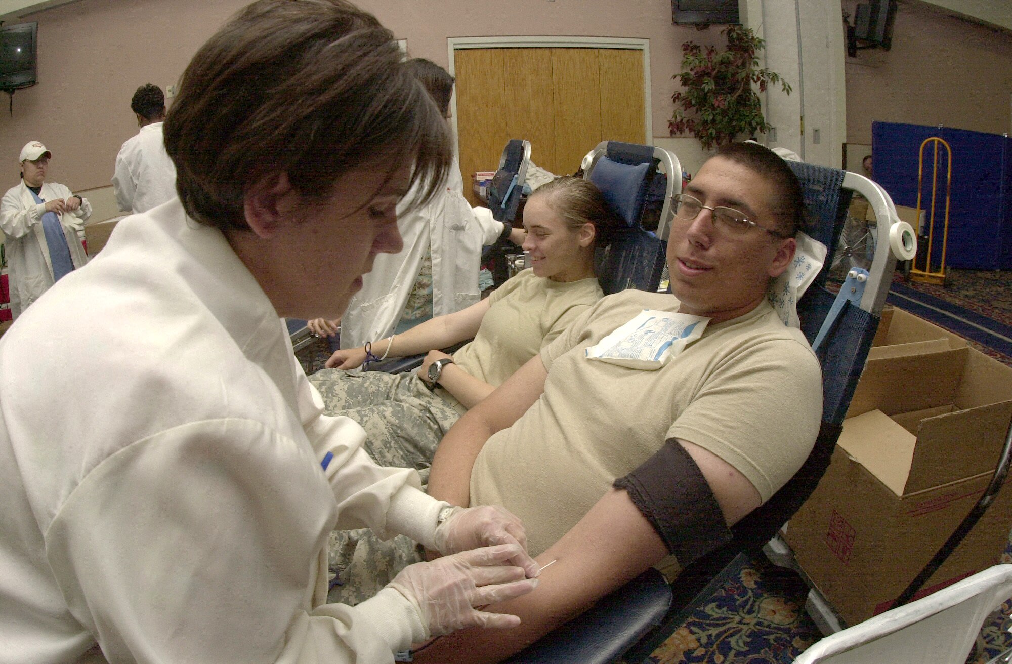 Army Private 1st Class Tyler Ladner, a student from the 344th Military Intelligence Battalion, watches as one of the donor care specialists from United Blood Services of San Angelo inserts a needle into his arm to begin collection of a blood unit Oct. 19. (U.S. Air Force photo by Airman 1st Class Luis Loza Gutierrez)