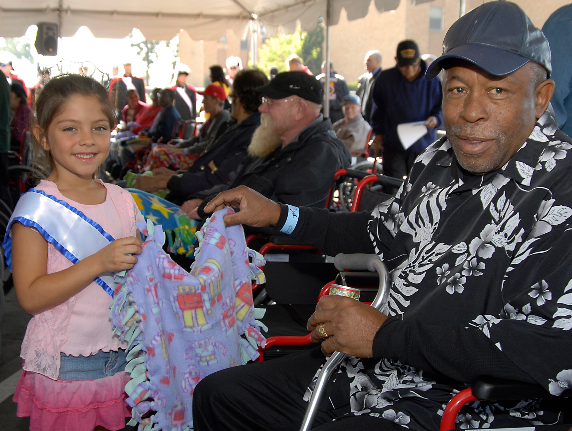 Gabriela Garcia gives a lap blanket to Army Veteran Ronald Totress. Los Angeles AFB Youth Services program participants and local Girl Scouts made lap blankets and a large greeting card, and presented them to veterans at the West Los Angeles Veterans Hospital, Nov. 10.  The event was held in conjunction with the Knights of Columbus presenting new wheelchairs to the vets at the hospital. (Photo by Joe Juarez)