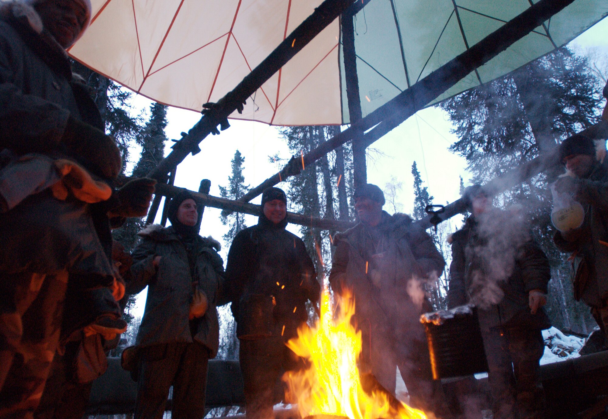 EIELSON AIR FORCE BASE, Alaska-- Various members of the U.S. Air Force assigned to Eielson and Elmendorf Air Force Bases, Alaska, stand under a canopy around a warm fire and discuss various topics while awaiting the start of the second day of the Arctic Survival Training Course on Nov. 15, 2007. The survival course teaches members how to survive in a severe cold climate. The course consists of shelter building, identifying safe food found in nature, how to stay warm, and how to correctly signal for help. The Arctic Survival Course is conducted at Eielson AFB by the members of Det. 1, 66 Training Squadron. (U.S Air Force photo by Staff Sgt Eric T. Sheler)