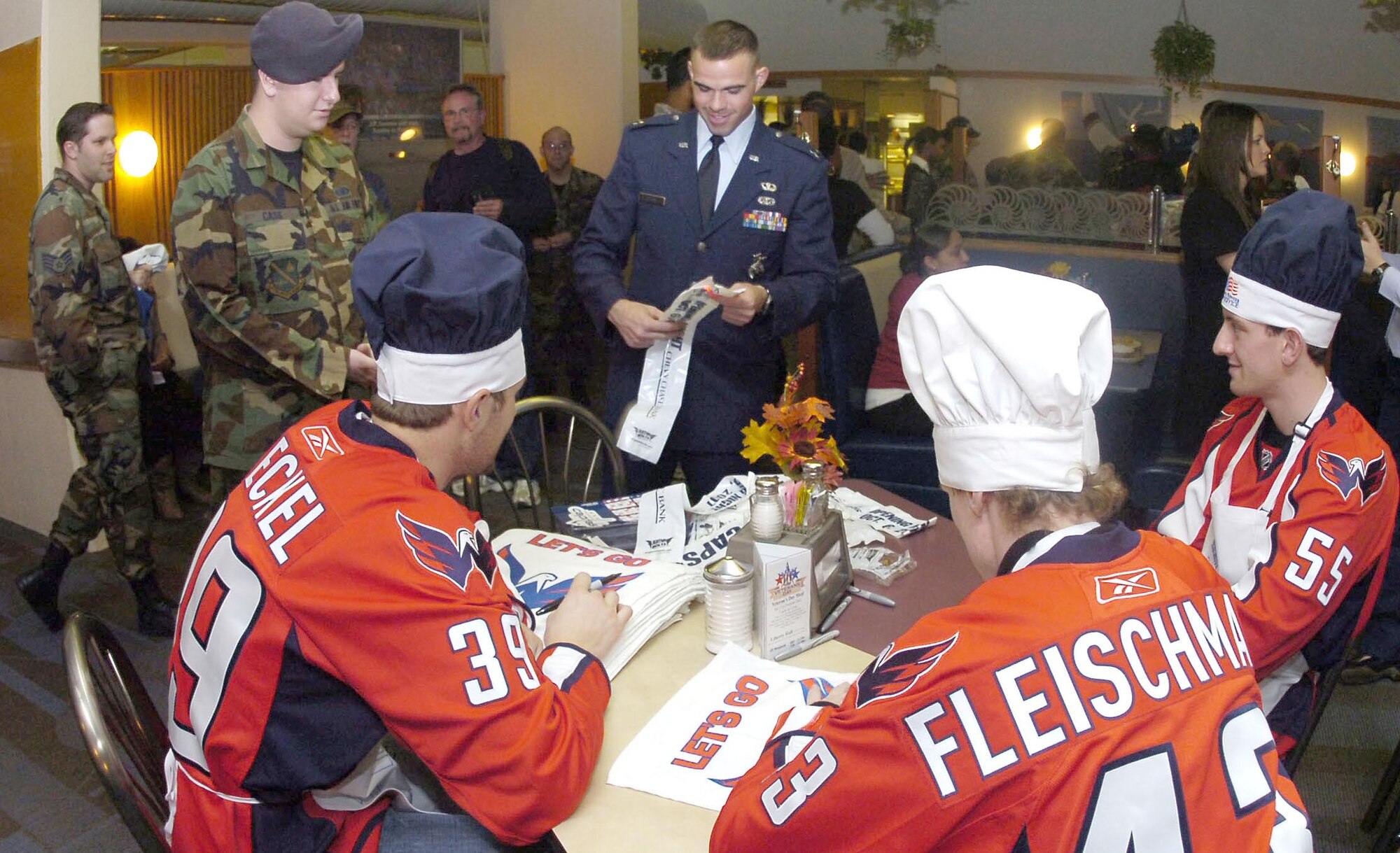 David Steckel, Thomas Fleishmann, and Jeff Schultz sign posters at the Freedom Hall Dining Facility after serving dinner on Nov. 13. Members from the Washington Wizards and Washington Capitals came to Andrews to visit with servicemember at various facilities. Their tour also included the Aeromedical Staging Flight at Malcolm Grow Medical Center. (US Air Force/Bobby Jones)