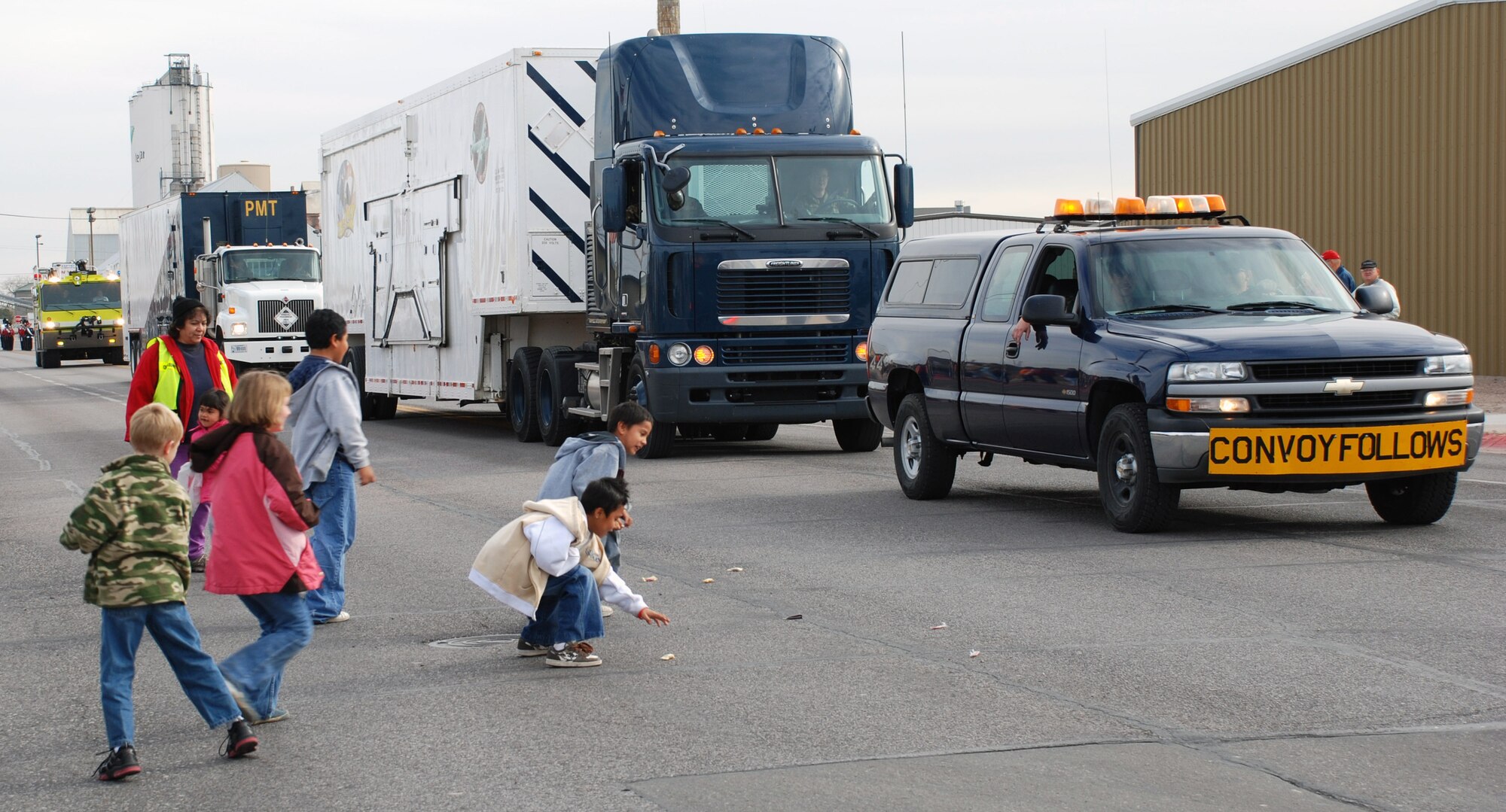 Children race into the street to grab candy and wave to the passing 90th Maintenance Group convoy for the Veterans Day parade. The convoy included a lead pickup, payload transporter and periodic maintenance truck as well as a Bearcat armored vehicle from 90th Security Forces Group (Photo by 2nd Lt. Lisa Meiman).