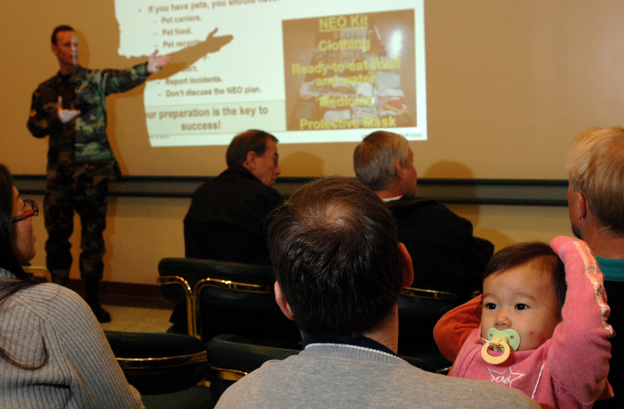 KUNSAN AIR BASE, South Korea – Scott Watson, a financial management systems analysis from the 8th Comptrollers Squadron, holds his daughter Pamela while receiving a noncombatant evacuation operations (NEO) situation briefing from Master Sgt. John McCraw, a NEO situations briefer during Courageous Channel here Nov. 16.  Courageous Channel is a semi-annual NEO exercise conducted to test the command's plans and procedures for a short-notice evacuation from the Republic of Korea.  (U.S. Air Force photo/ TSgt Quinton T. Burris)