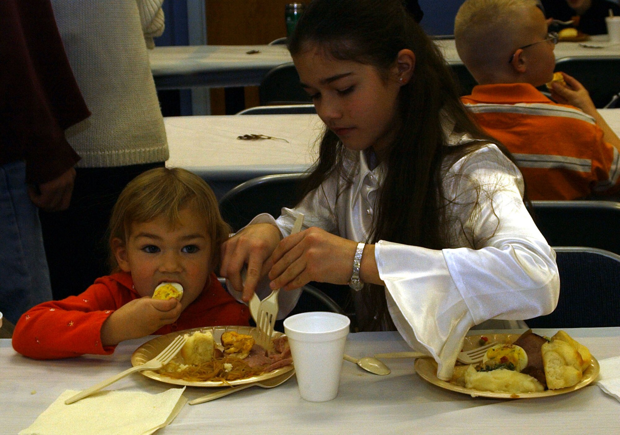Little Warrior Sophia, 3, tries out a deviled egg while her big sister Victoria, 11, cuts her ham. The two were enjoying the feast put on by the Catholic and Protestant communities of Malmstrom at the annual Thanksgiving dinner Sunday at the Chapel Annex. (U.S. Air Force photo/Valerie Mullett) 