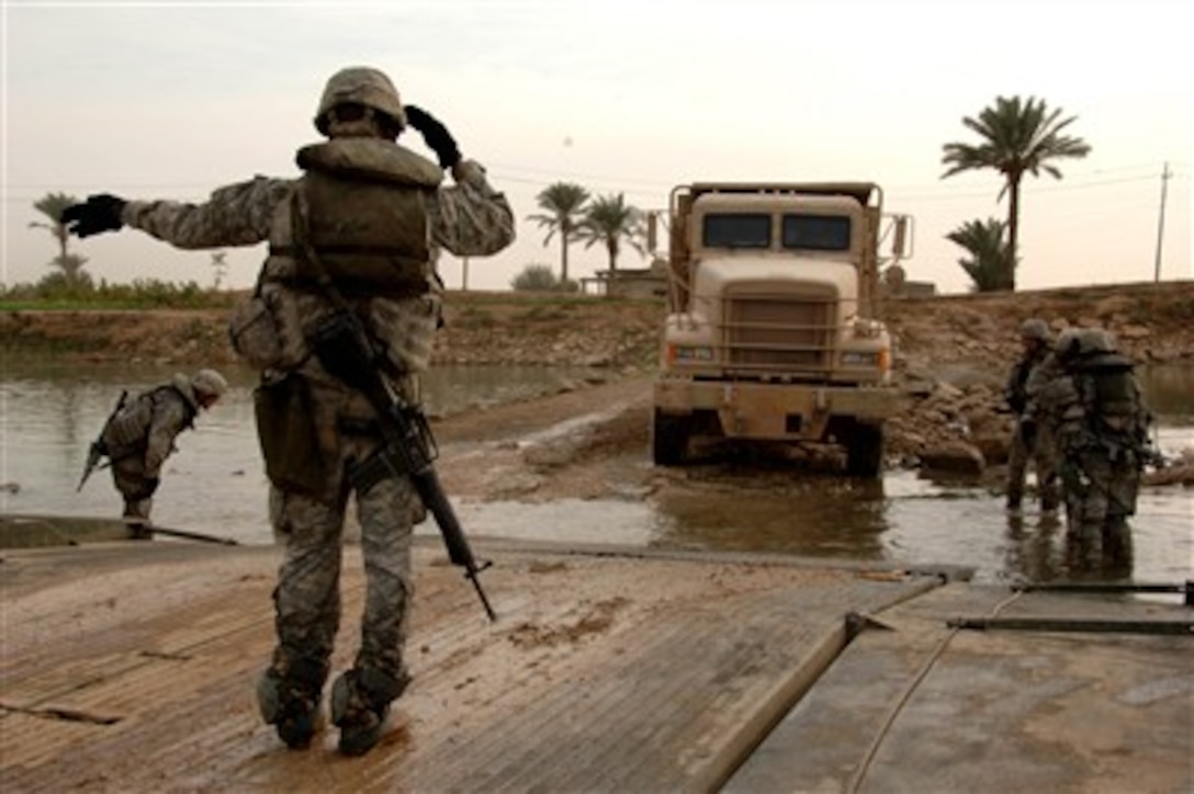 A U.S. Army soldier directs the driver of a truck onto a floating bridge as soldiers from the 20th Engineer Brigade shuttle vehicles across the Euphrates River near Baghdad, Iraq, on Nov. 16, 2007. 