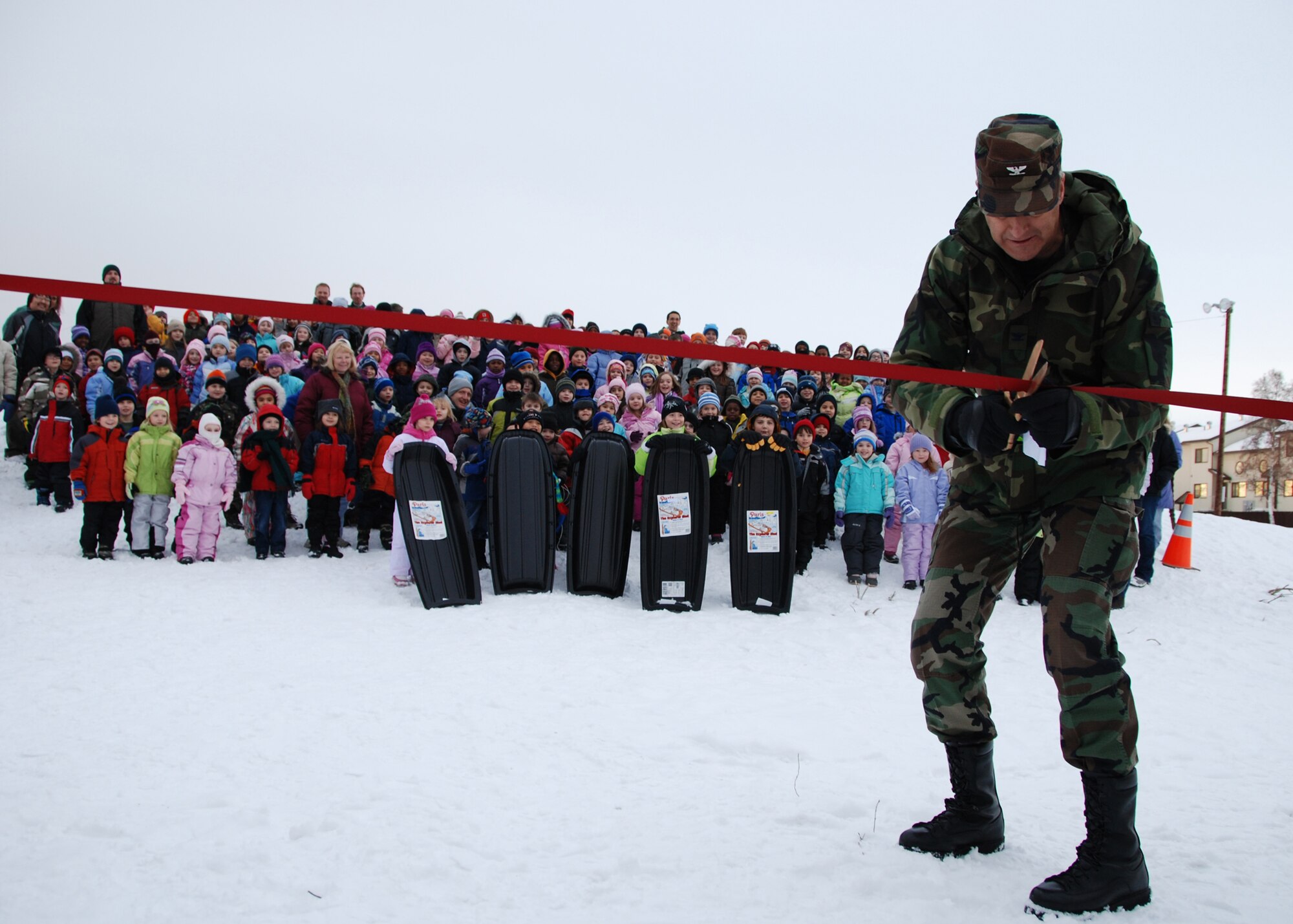 EIELSON AIR FORCE BASE, Alaska-- Col. Brian Maas, 354th Fighter Wing deputy commander, cuts the ribbon to officially open the new sled hill  Nov. 20 behind Anderson Elementary School. Around 300 AES students attended the ceremony and five won sleds to be the first to sled down the hill. The sled hill was build by civilian contractors: Great Northwest, Inc., MWH and DGR. (U.S. Air Force photo by Airman 1st Class Nora Anton)