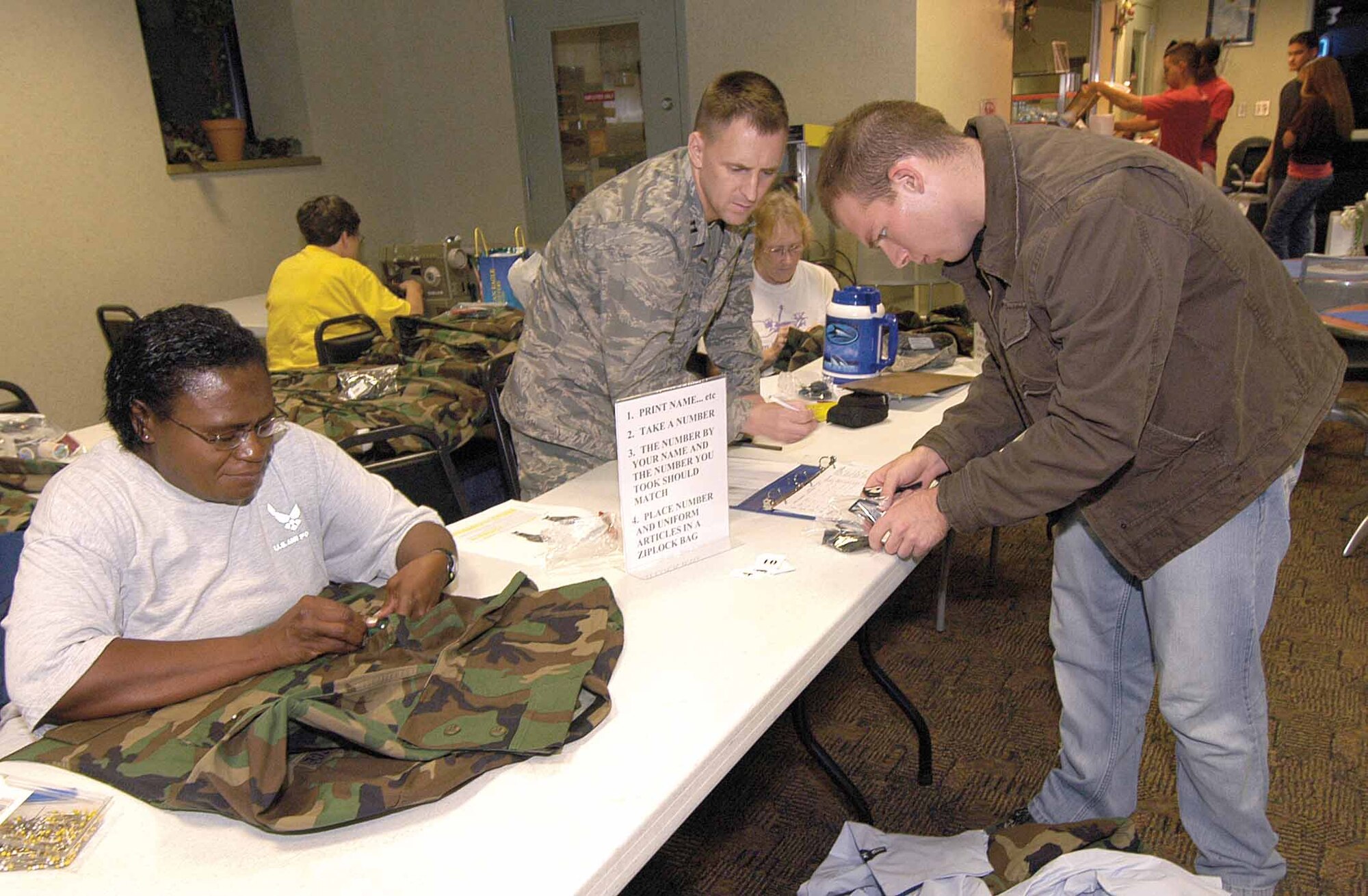 Approximately 13 Airmen took advantage of free food and free patch sewing for the Base Chapel-sponsored Munch and Mend at the Vanwey Recreation Center. Chaplain (Capt.) Martin Booth signs in an Airman Nov. 13 while volunteers, including Master Sgt. Mavis Durant, 72nd Medical Group Optometry Clinic, work on uniforms. (Air Force photo by Margo Wright)