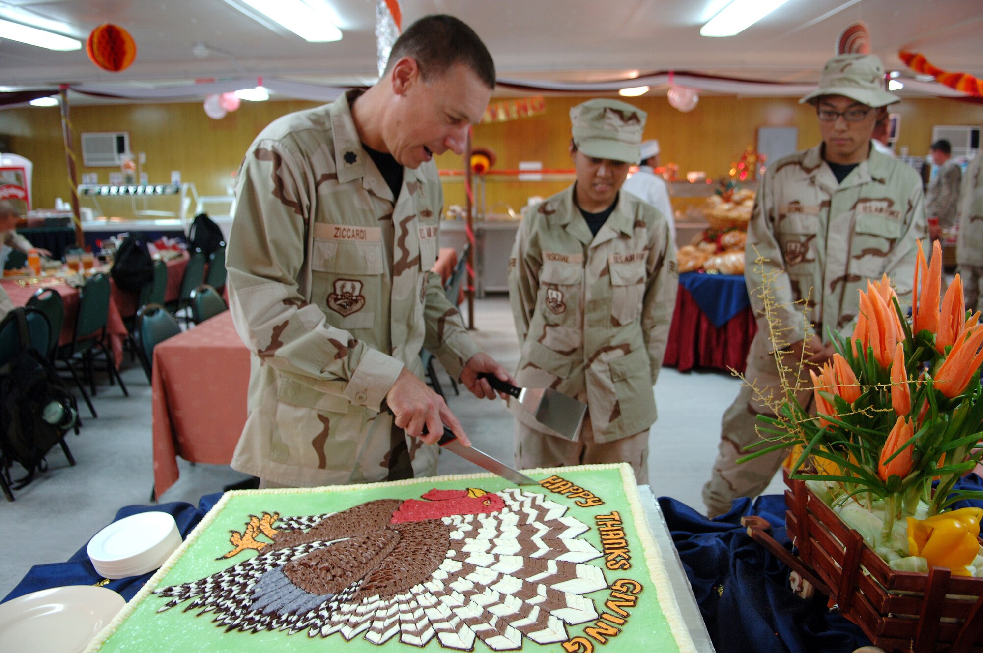 SOUTHWEST ASIA - Chaplain (Lt. Col.) Gary Ziccardi, 379th Air Expeditionary Wing chaplain, cuts the Thanksgiving Day cake Nov. 22 as Senior Airman Nikky Pascual, and Airman 1st Class June Seong, 379th Expedtionary Services Squadron, stand by at the Independence Dining Facility at a Southwest Asia air base.  Both Airmen are deployed from Nellis AFB, Nev. Airman Pascual is from Honolulu, Hawaii, and Airman Seong is from Tae-jeon, Korea. (U.S. Air Force Photo/Master Sgt. Greg Kunkle)