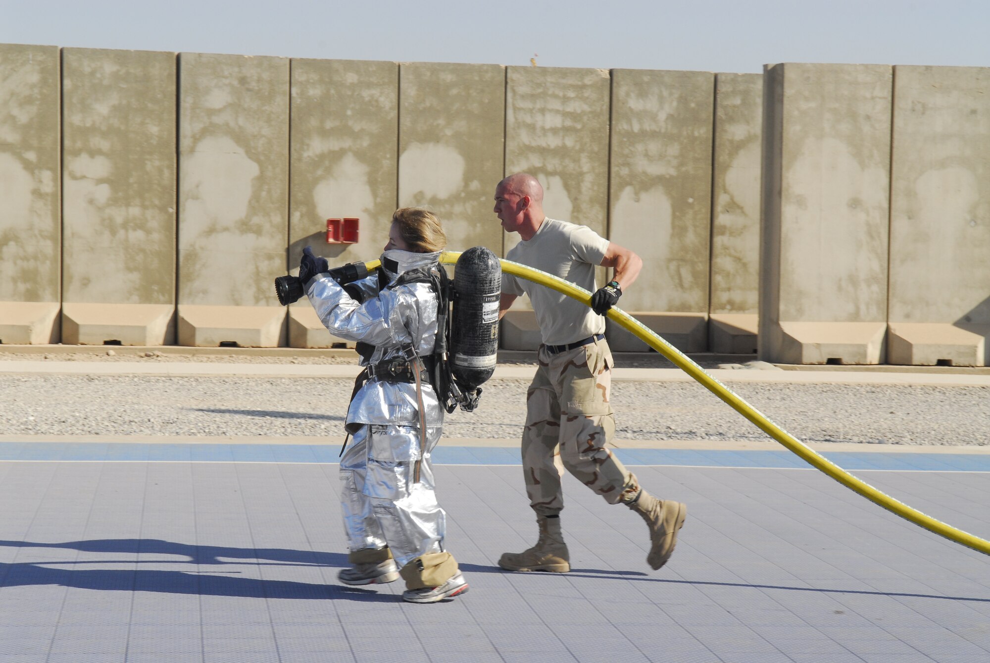BALAD AIR BASE, Iraq -- Capt. Deborah Travis, 732nd Expeditionary Support Squadron director of operations, prepares to use a fire hose as Senior Airman Paul Rosato, 332nd Expeditionary Civil Engineer Squadron, makes sure she safely operates the hose. The firefighters aided all participants throughout the event ensuring safety. Captain Travis is deployed from Langley Air Force Base, Va. and Airman Rosato is deployed from Aviano Air Base, Italy. (U.S. Air Force photo/Staff Sgt. Joshua Garcia)