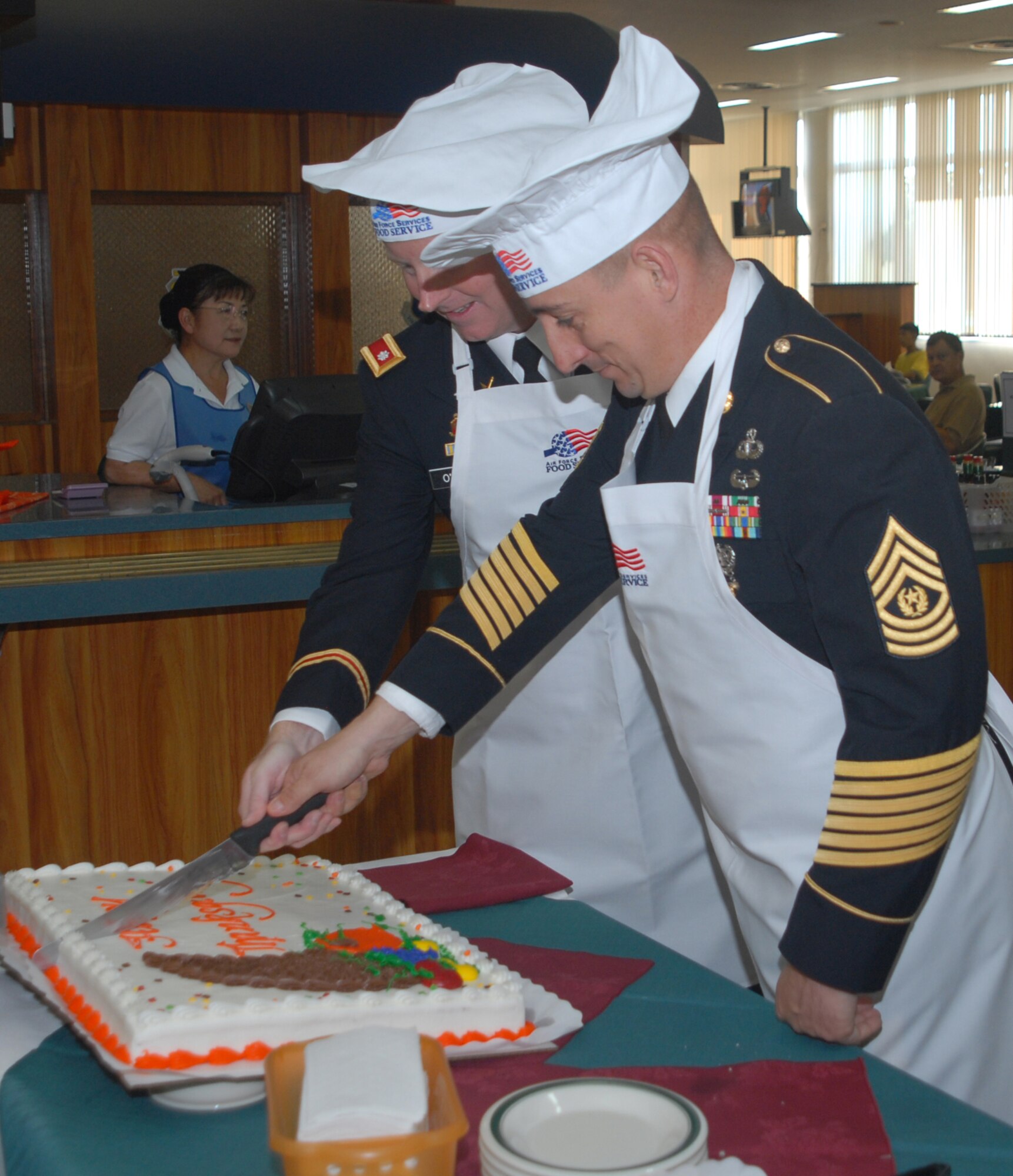 Army Lt. Col. Edward O'Neal, 1-1 Air Defense Artillery Battalion commander, and Command Sgt. Maj. Michael Kuppers cut a Thanksgiving cake at the Kadena Air Base, Japan, Marshall Dining Facility, Nov. 22, 2007. Several commanders and senior NCOs served lunch to dining facility patrons to thank them for their contributions to the mission. 
