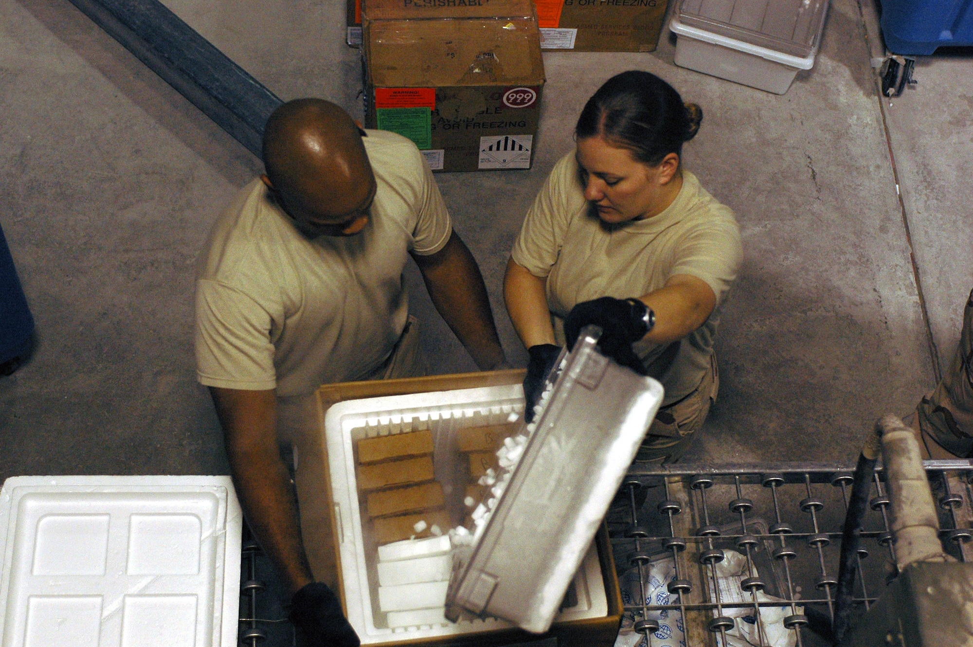 Tech. Sgt. Joseph Pinkney (left) holds a box of fresh frozen plasma steady as Senior Airman Beth Gunn pours more dry ice into the box Nov. 20. Fresh frozen plasma must be kept frozen to prevent spoiling of the blood product.  Sergeant Pinkney and Airman Gunn are with the 379th Expeditionary Medical Group's blood transshipment center and are deployed from Langley Air Force Base, Va. (U.S. Air Force photo/Staff Sgt. Jason Barebo) 