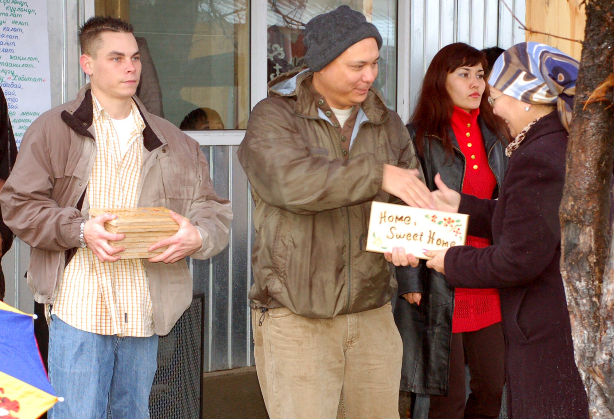 Tech. Sgt. Richard Kilton presents a housewarming plaque to one of the new Habitat for Humanity homeowners Nov. 23  in Bishkek, Kyrgyzstan, while Airman 1st Class Brandon Edwards assists. Sergeant Kilton is a 376th Expeditionary Security Forces Squadron vehicle control officer at Manas Air Base, Kyrgyzstan, and the Habitat for Humanity focus group leader. Airman Edwards is with the 376th Expeditonary Logistics Squadron. Manas AB Airmen logged more than 1,5000 hours helping to complete the project for the new home owners. (U.S.Air Force photo/Staff Sgt. Giana Jaworski) 
