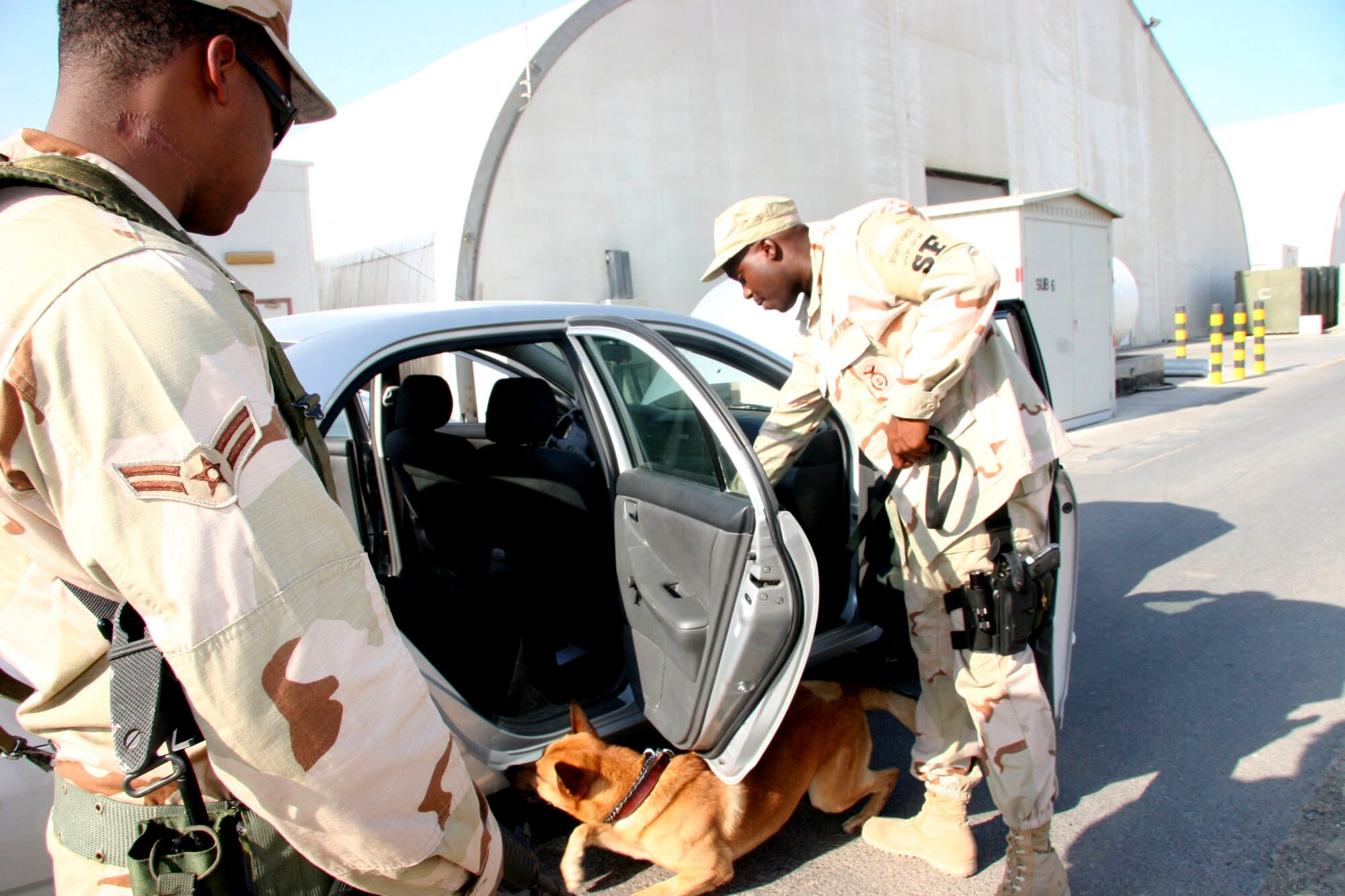 Staff Sgt. Malik Calhoun, 380th Expeditionary Security Forces Squadron K-9 handler, and Arco, his patrol and explosive detection dog, conduct a vehicle sweep while his brother Airman 1st Class Dandre Bufford provides overwatch during an explosive detection training scenario Nov. 27. (U.S. Air Force photo/Master Sgt. Ruby Zarzyczny) 
