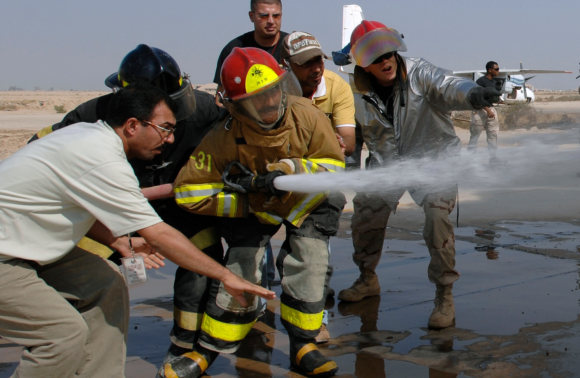 A local Iraqi firefighter operates a hose while Staff Sgt. Joshua Wilson gives advice to effectively knock out a fire during training. The 407th Expeditionary Civil Engineer Squadron firefighters conduct a live-fire training exercise for the Iraqi firefighters teaching basic skills of advancing a hand line, procedures on approaching hazardous environments and performing search and rescue. Sergeant Wilson is deployed from Kadena Air Base, Japan. (U.S. Air Force photo/Airman 1st Class Jonathan Snyder)