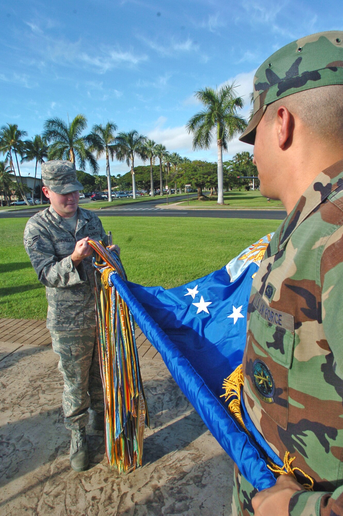 Senior Airman Donald Rochin, Pacific Air Forces Air Intelligence Squadron holds the Air Force guidon as Airman 1st Class Steve Shiveley, 17th Air Weather Squadron unfurls the battle streamers Tuesday. Both Airmen are part of an all-Pacific Air Forces honor guard team preparing for the PACAF change of command scheduled for Friday at 4 p.m. (U.S. Air Force photo/Mark Munsey)

