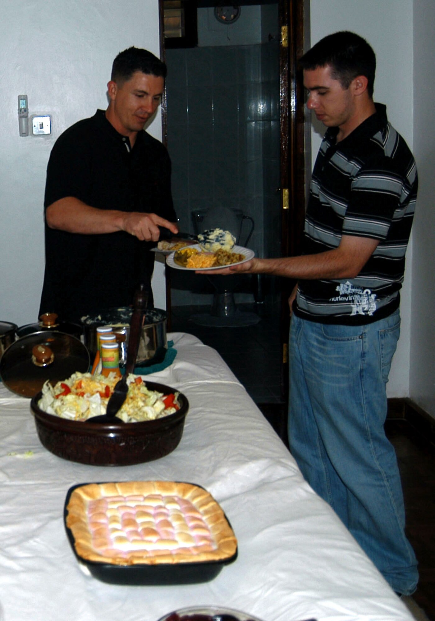 Navy Chief Religious Programs Specialist Wayne M. George (left) piles on some traditional Thanksgiving foods onto Army Spc. Michael R. Johnston's plate at the house of a servicemember assigned to the U.S. Embassy in Tanzania who invited more than 20 people to his house to celebrate the holiday. Mr. George, a Bloomfield, N.M., native, is the Chaplains Department senior enlisted leader assigned to the Combined Joint Task Force-Horn of Africa. Specialist Johnston, a Tulsa, Okla., native, is a civil affairs specialist assigned to Civil Affairs Team 11 of C Company, 486th Civil Affairs Battalion. (U.S. Air Force photo/Staff Sgt. Jennifer Redente)