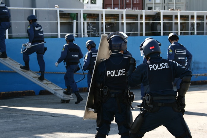 Under the eyes of Marines and Iwakuni local officials, Yamaguchi Prefecture riot specialists board a vessel in search of armed terrorists as part of an annual bilateral training exercise at the Iwakuni Port Nov. 28. The exercise is conducted to foster interoperability between the Japanese Coast Guard and local law enforcement, polishing procedures to be utilized in the adverse event of a terrorist attack. Marines were invited to the event to take note of the Japanese protocol and to become familiar with its tactics and procedures should such a calamity require the side-by-side efforts of both Marines and Japanese defense agencies.