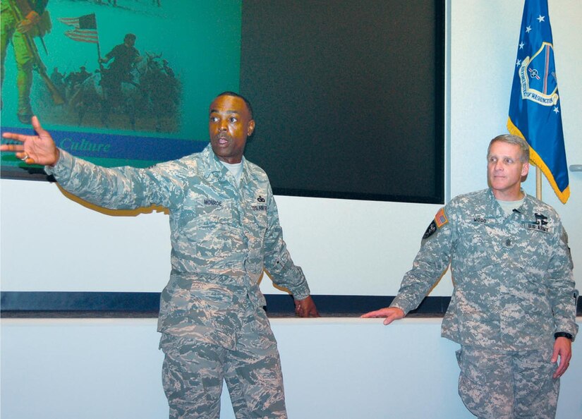 Air Force District of Washington Command Chief Master Sergeant, Chief Master Sgt. Lew Monroe, left, gestures to the seated wing command chief master sergeants as he joins Army Command Sgt. Maj. Dan Wood, command senior enlisted leader for both U.S. Northern Command and the North American Aerospace Defense Command, at the stage in the Brig. Gen. Jimmy Stewart Theater on Bolling AFB, D.C., Monday.  Sergeant Major Wood briefed AFDW-based senior noncommissioned officers Monday afternoon following a day visiting AFDW Airmen and units at Andrews AFB, Md., and Bolling. "Every bit of what NORTHCOM does is about defense of our homeland," Sergeant Major Wood said. He charged SNCOs with, among other things, leading the effort to be on the lookout for and ready to respond to dangers in the AFDW area of operations. "We ought to have a culture of preparedness in our nation," he said.  "Uniformed service members ought to take the lead.  We ought to be leaning forward in the foxhole." (US Air Force/SMSgt Michael Land)