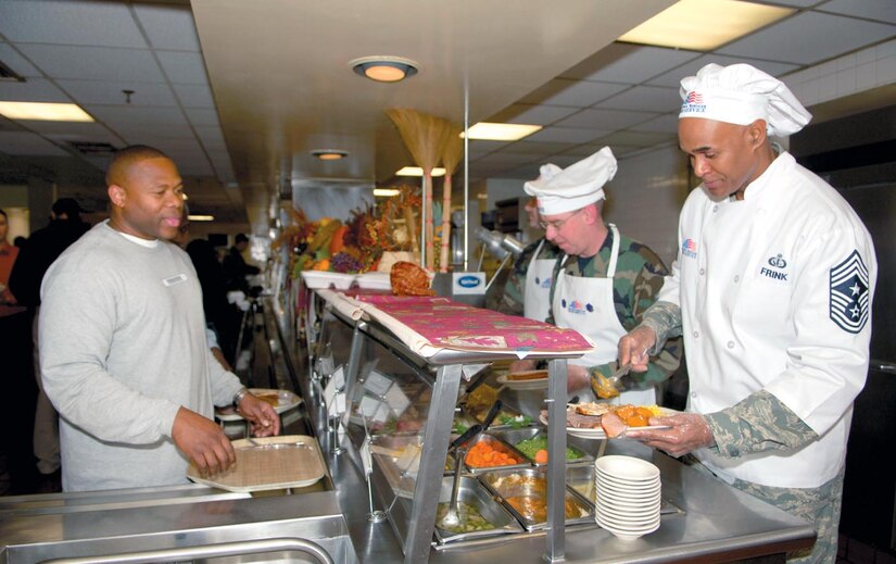 Chief Master Sgt. Leroy Frink, 316th Wing Command Chief Master Sergeant, and Master Sgt. James Matthews, 316th Mission Support Squadron first sergeant, serve Navy Petty Officer 1st Class James Kelly Thanksgiving dinner at the Freedom Hall Dining Facility Nov. 22. Leadership from various wings and squadrons arrived at the dining facility to serve servicemembers who could not visit home for the holiday, a hot meal.
(US Air Force/TSgt Christopher Matthews)