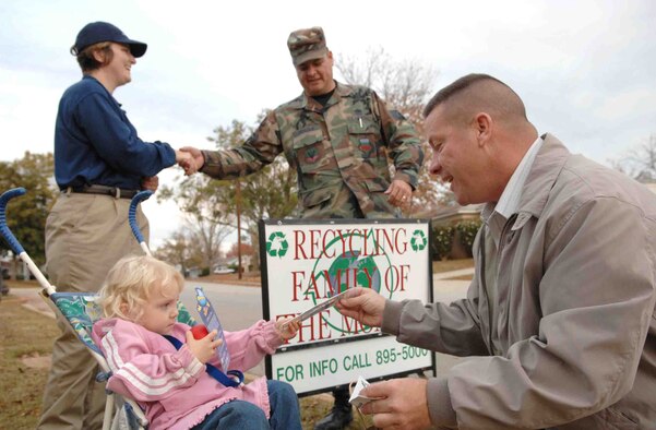 SHAW AIR FORCE BASE, S.C. -- Mark Hall, 20th Civil Engineer Squadron pollution prevention planner, shows the contents of a gift package to 2-year-old Amelie Helbing as Tech. Sgt. Andrew Teague, 20th CES environmental plans overseer, congratulates Staff Sgt. Nicole Helbing, 20th Foward Support Squadron fitness shift supervisor, for winning the Recycling Family of the Month Award Nov. 27. (U.S. Air Force photo/Airman 1st Class Kathrine McDowell)