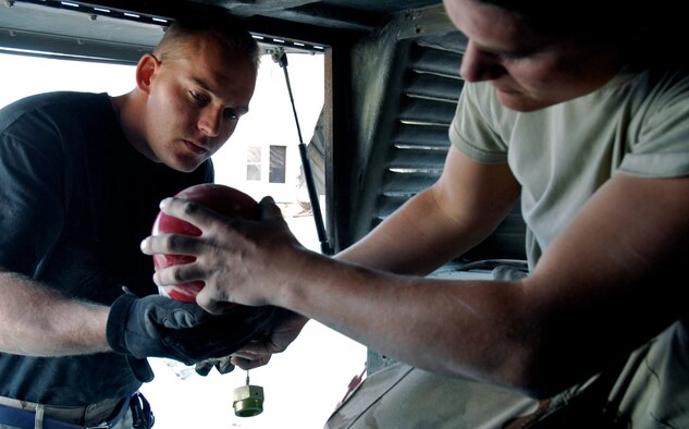 Staff Sgt. Benjamin Johnson hands Senior Airman Josh Theunissen a component of a fire suppression system to install into a Humvee Nov. 27. Both are members of Frag Team 5, which is responsible for installing up-armor kits, fire suppression systems, improved seat belts and gunner restraints in Air Force combat vehicles. (U.S. Air Force photo/Staff Sgt. Joshua T. Jasper)