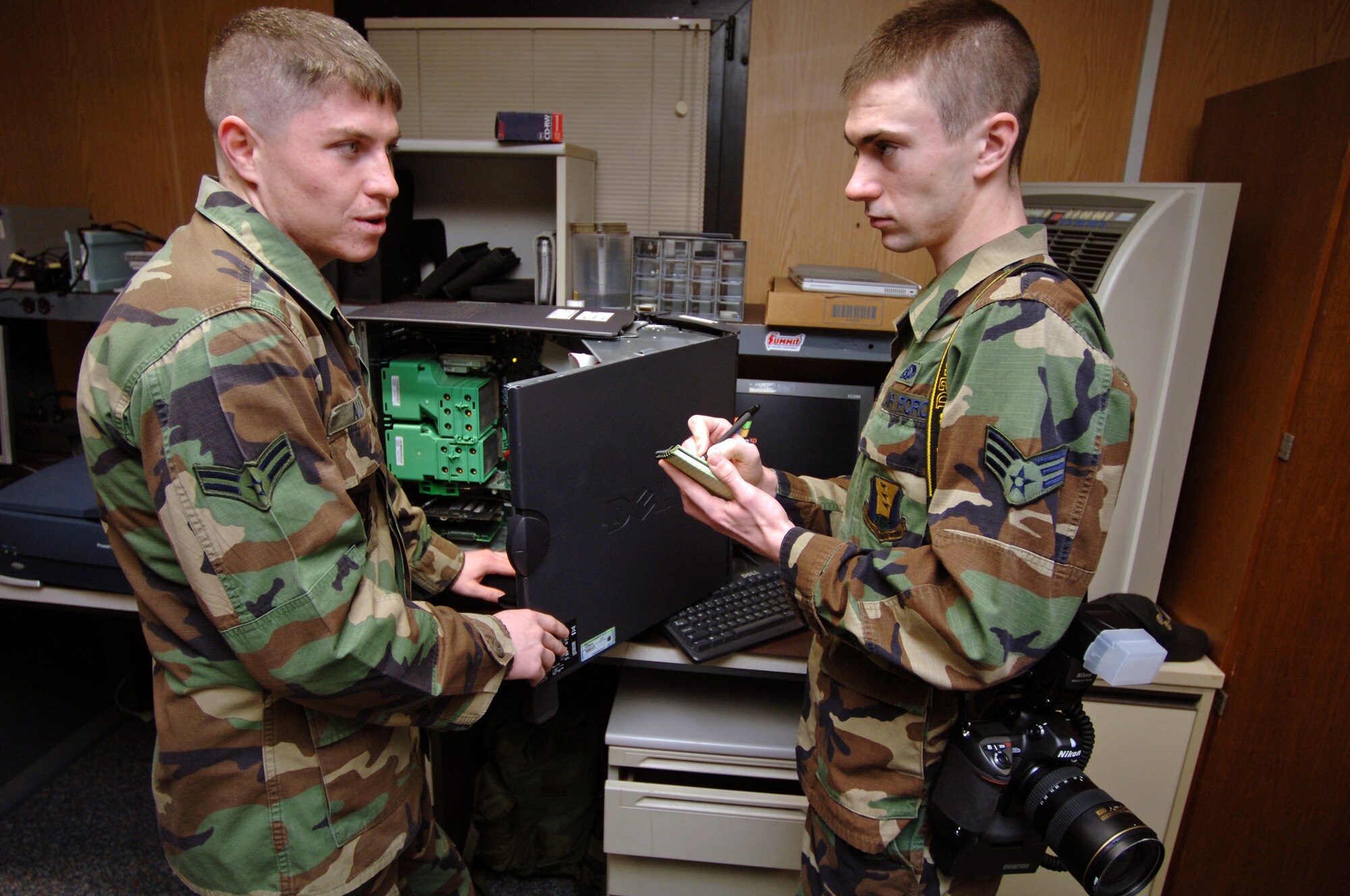 Senior Airman Levi Riendeau, 435th Air Base Wing Public Affairs still photographer, interviews Airman 1st Class Branan Allen, 86th Contingency Response Group information manager, while he replaces video cards in a government computer on Ramstein Air Base, Germany, Nov. 29.  Airman Riendeau has recently begun to write stories to accompany his photos as part of a public affairs/multimedia merge. (U.S. Air Force photo/Airman 1st Class Marc I. Lane)(Released)
